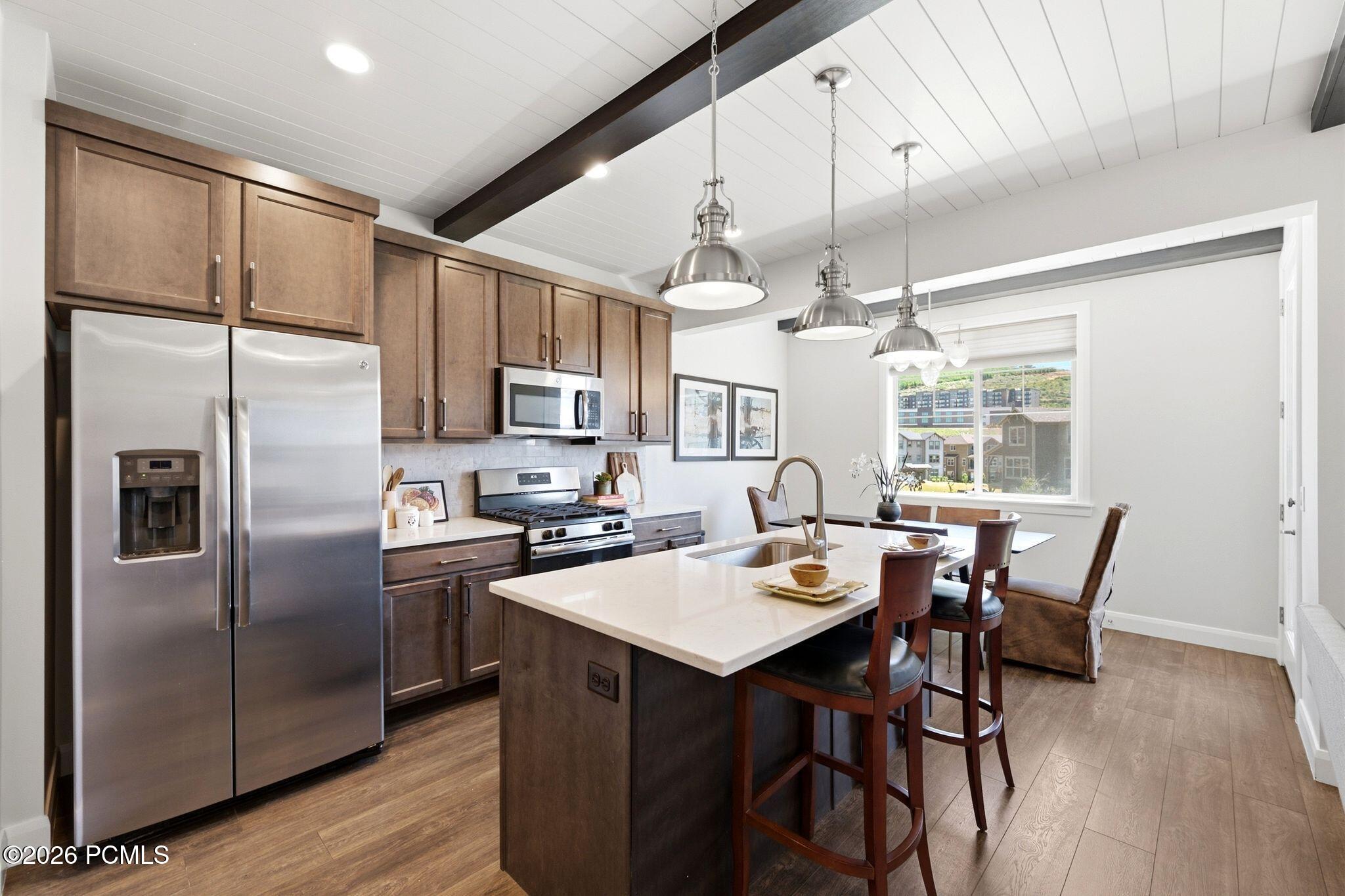 Modern kitchen featuring stainless steel appliances, wood-finish flooring, white shiplap ceiling with exposed beams, and a center island with pendant lighting