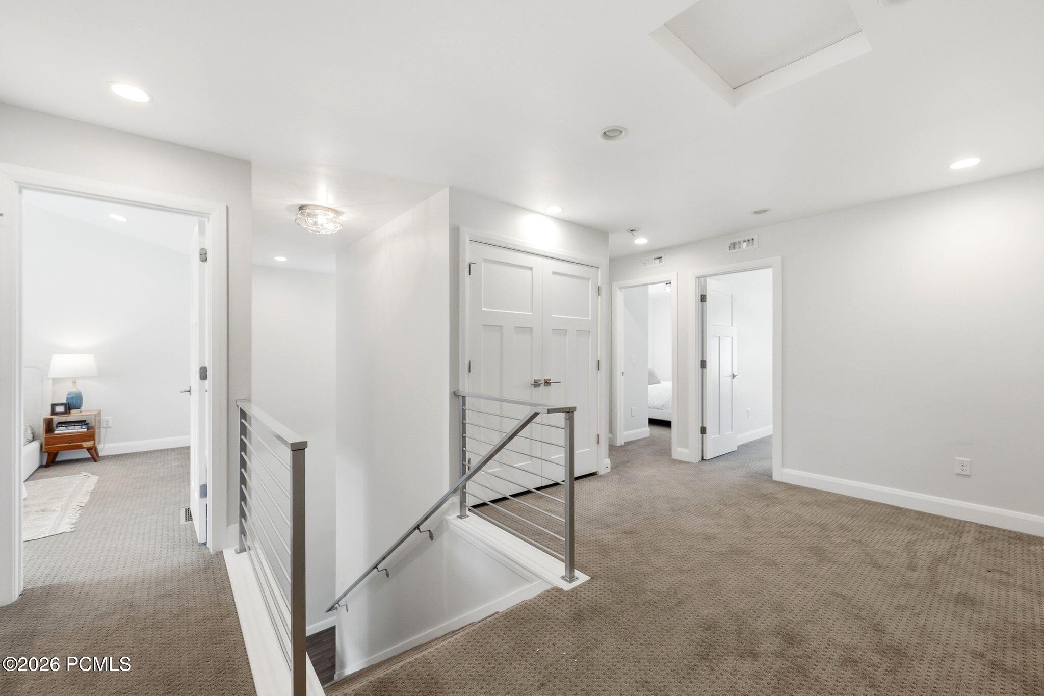 Upper-level landing featuring neutral carpeting, white walls, and recessed lighting