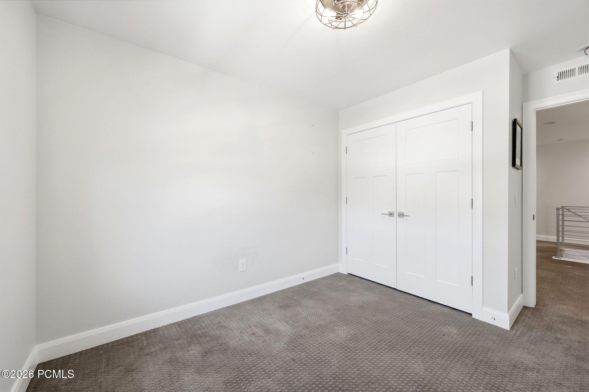 White paneled bifold doors, neutral wall paint, gray patterned carpeting, white baseboards, and a contemporary ceiling fixture