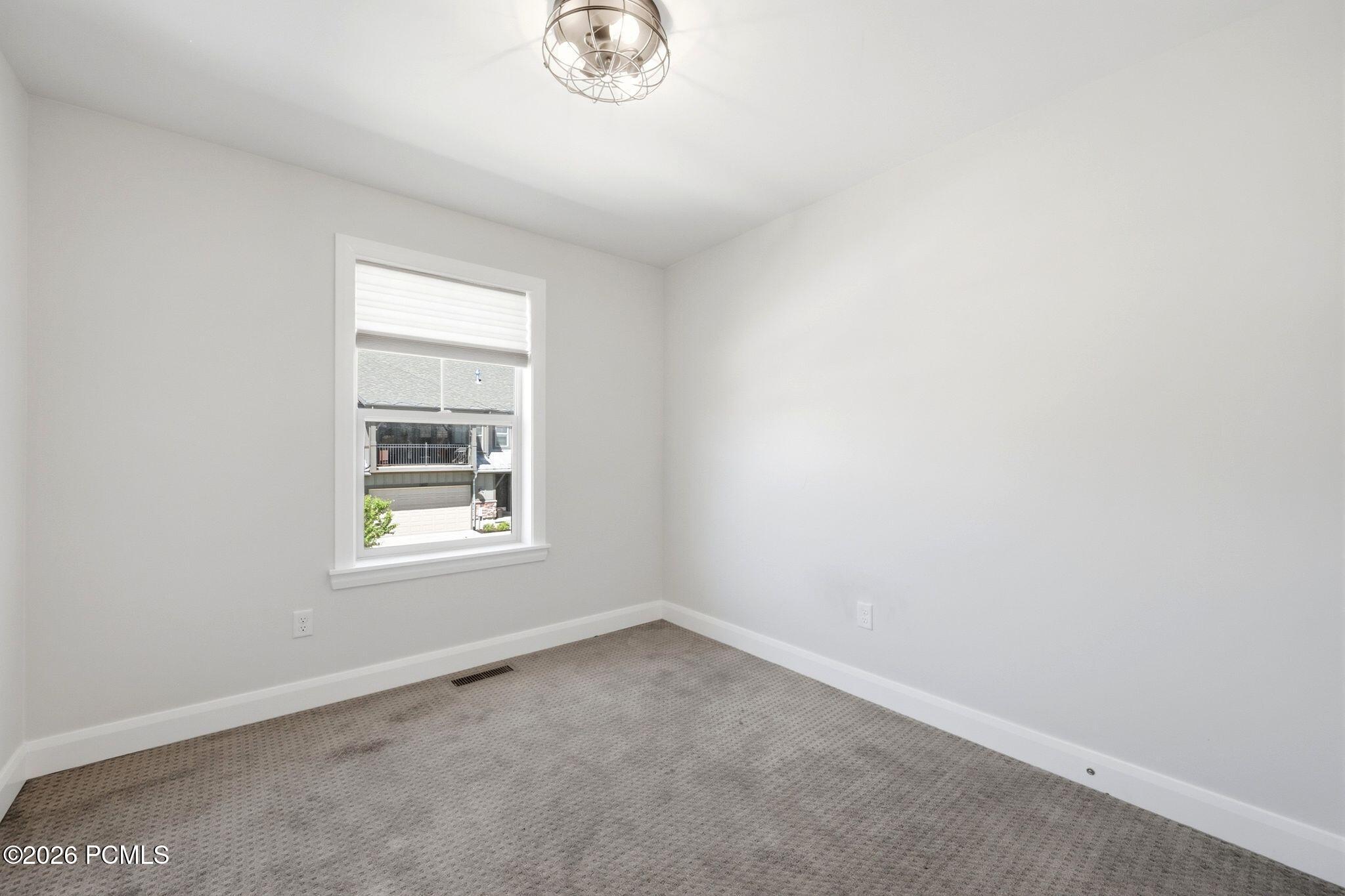 Neutral-toned room featuring a single window with white trim, gray patterned carpeting, and a modern ceiling light fixture