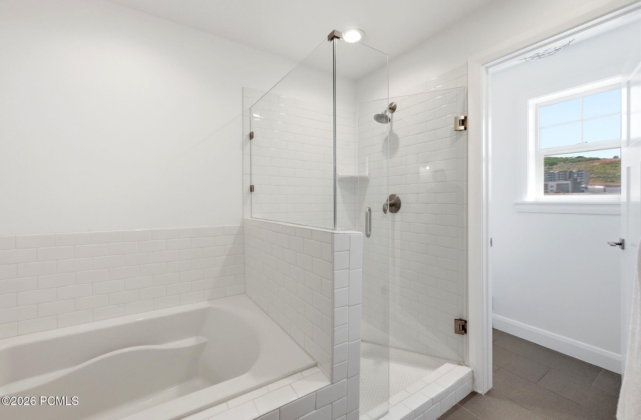 Bathroom featuring a full-size bathtub, glass-enclosed shower with subway tile surround, and matte nickel fixtures