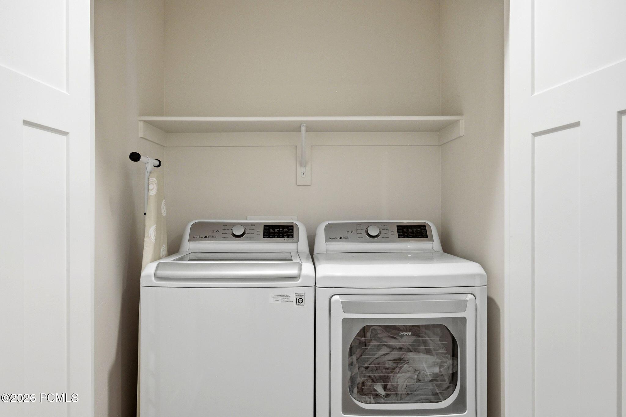 Dedicated laundry area featuring a built-in shelf, white paneled bifold doors, and neutral wall tones