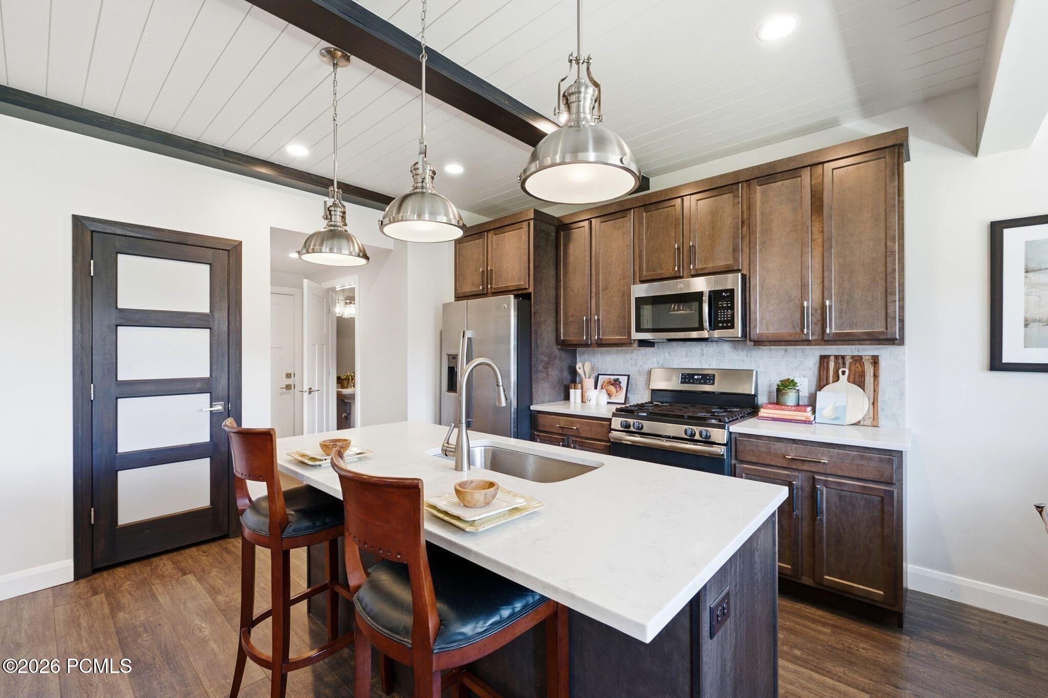 Kitchen featuring a large central island with seating, stainless steel appliances, dark wood-finish cabinetry, white countertops, and wood-finish flooring