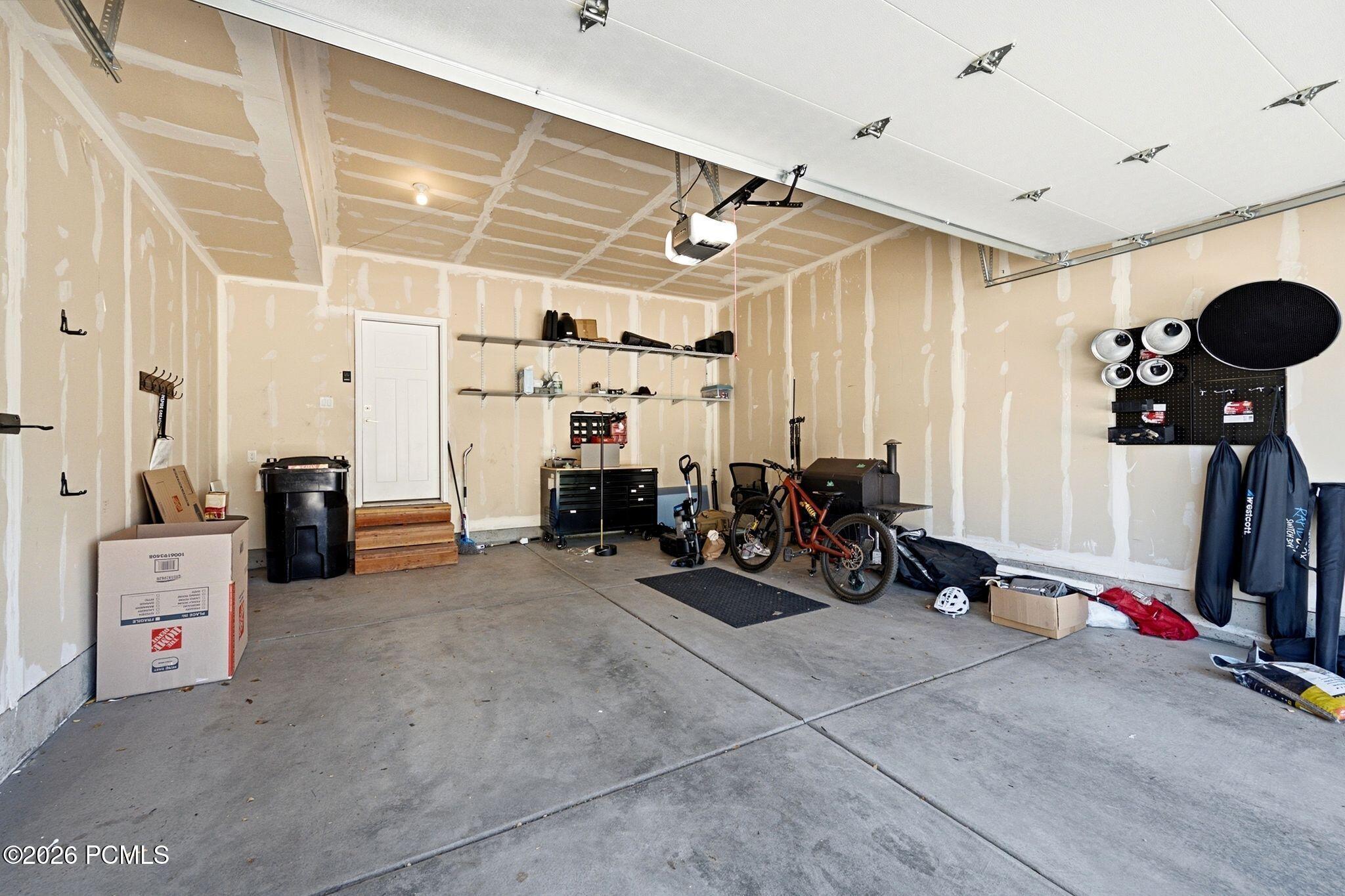 Spacious garage featuring a concrete floor, overhead garage door, built-in shelving, and interior access door