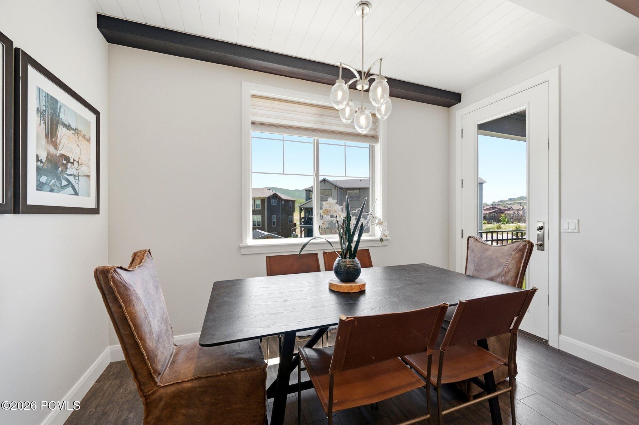 Dining area featuring wood-finish flooring, a contemporary chandelier, and a large window providing natural light