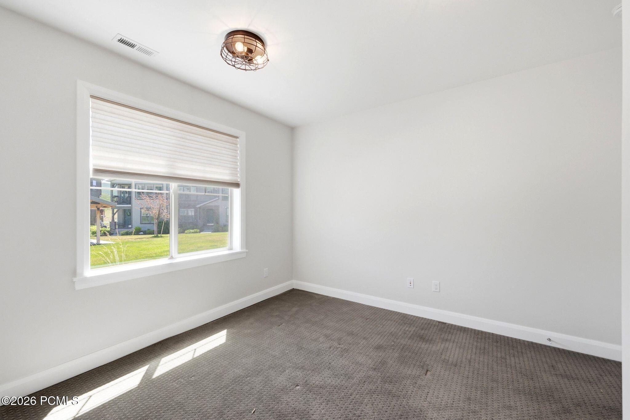 Carpeted interior room with white walls, a single window featuring window treatments, and a decorative ceiling light fixture