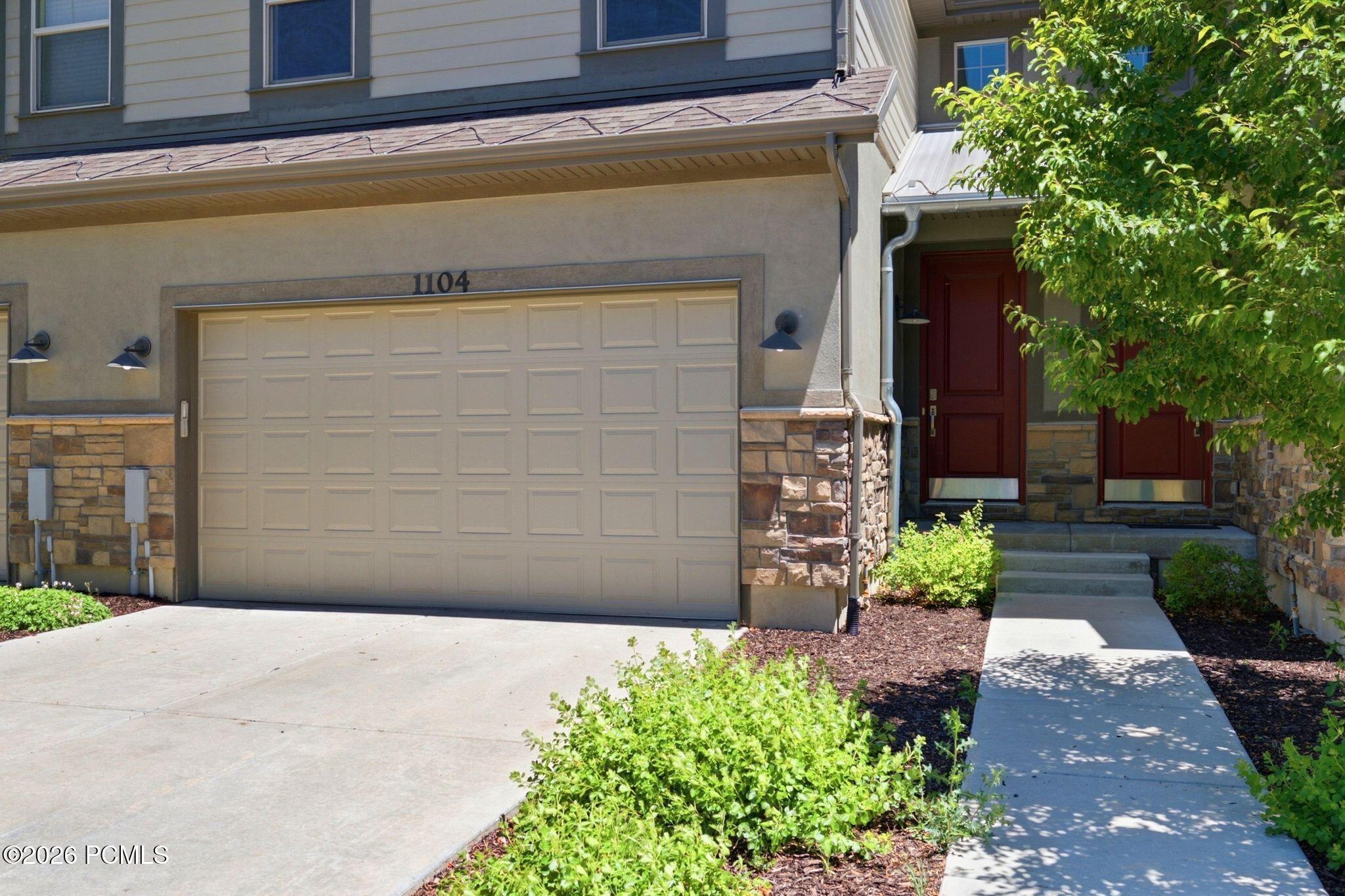 Townhome exterior featuring a paneled garage door, stone accents, and a red entry door