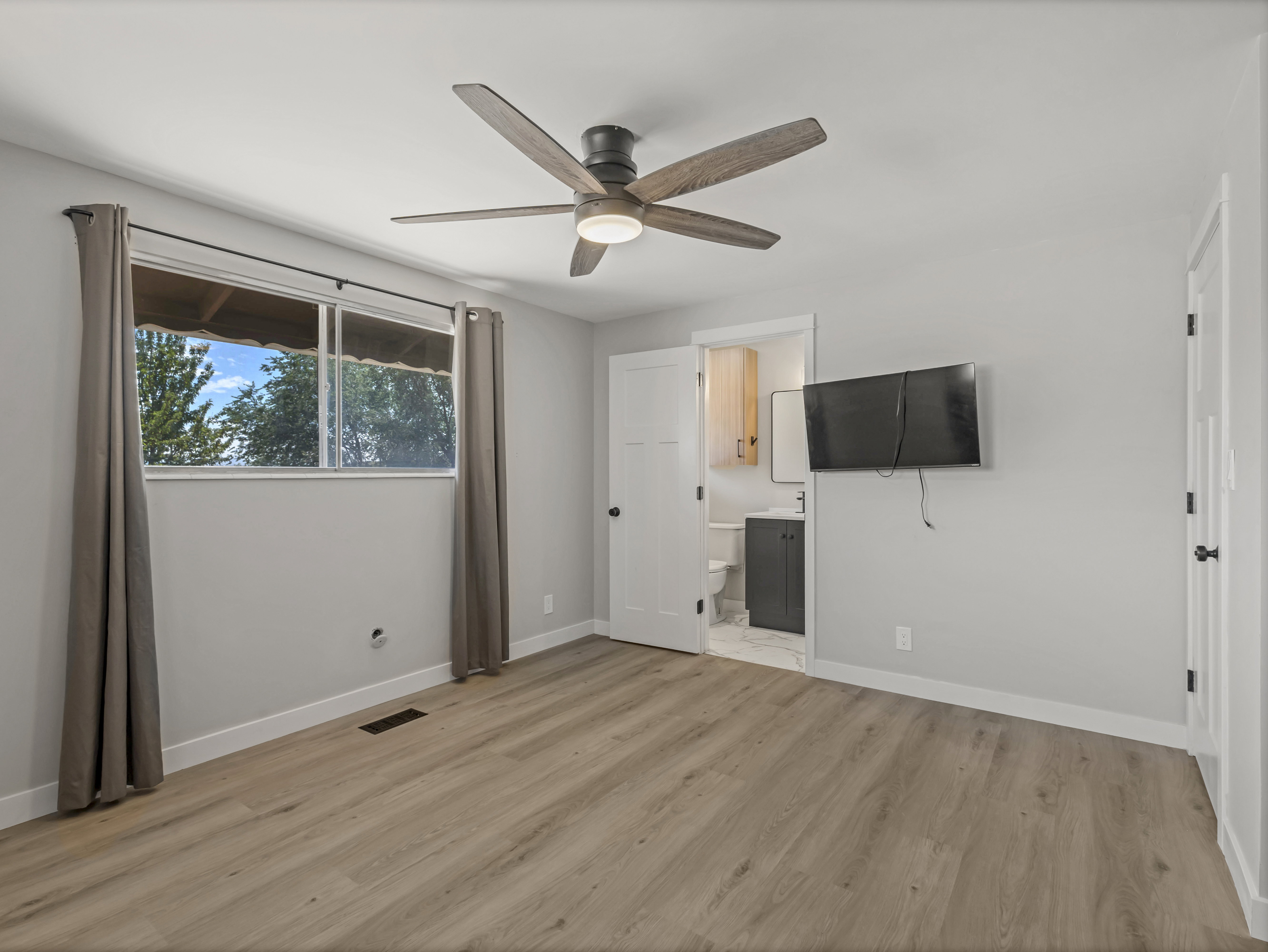 Spacious room featuring wood-finish flooring, a contemporary ceiling fan with integrated lighting, and a large window