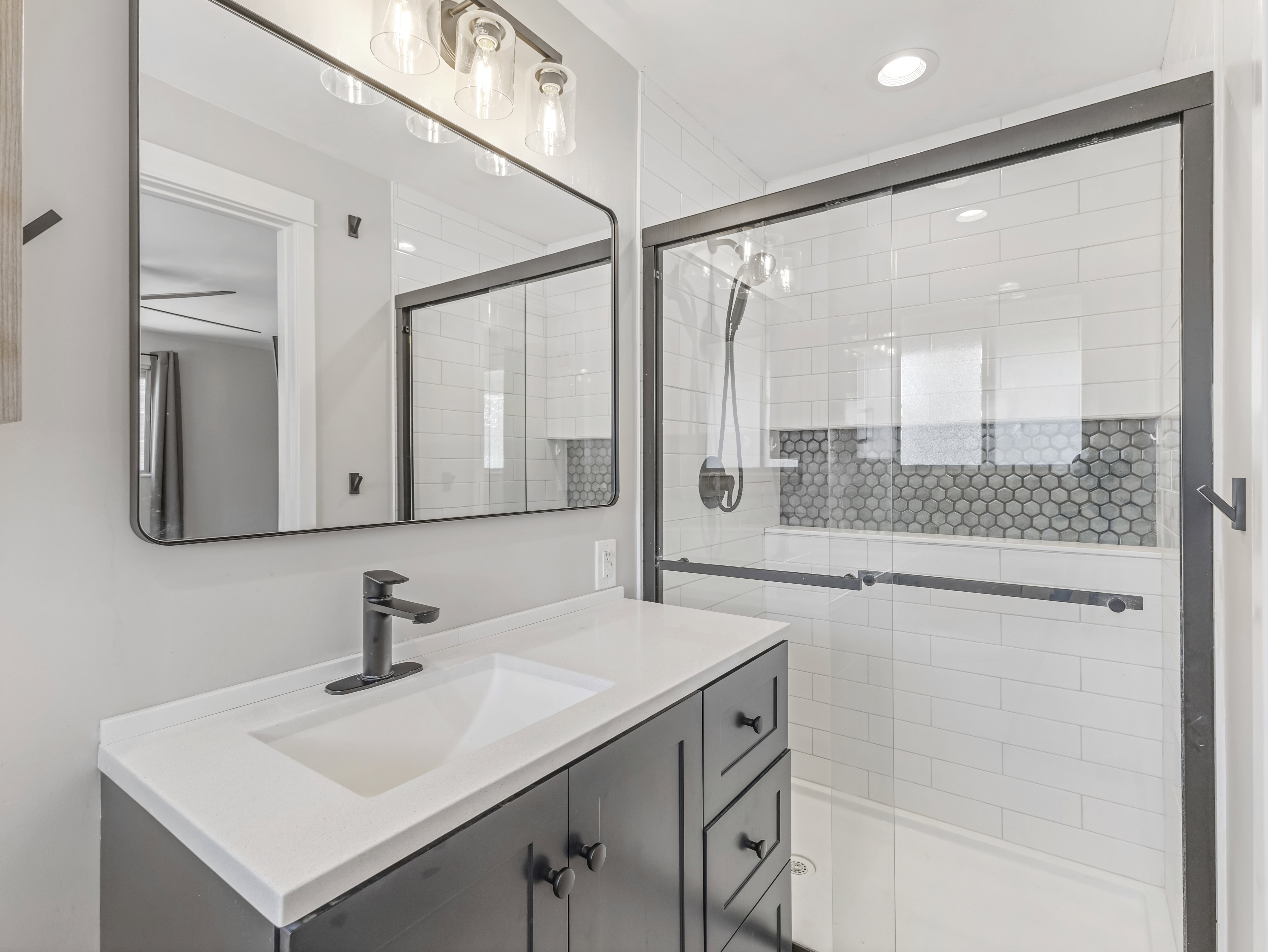 Bathroom featuring a dark wood-finish vanity with a white countertop and integrated sink, a rectangular mirror, and a glass-enclosed shower with subway tile and penny tile accents