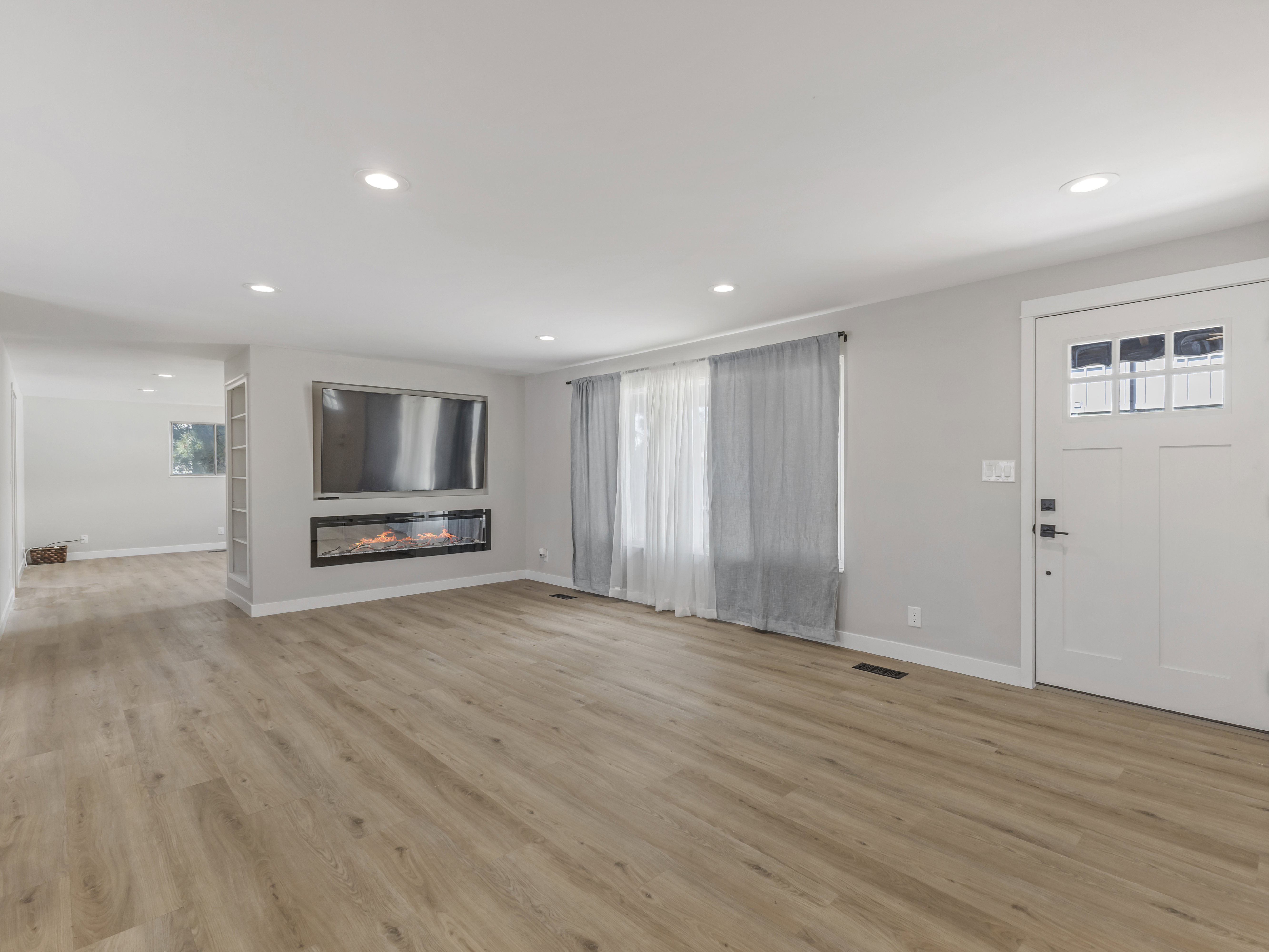 Open-concept living space featuring wood-finish flooring, recessed lighting, a modern built-in electric fireplace, and a multipaneled entry door