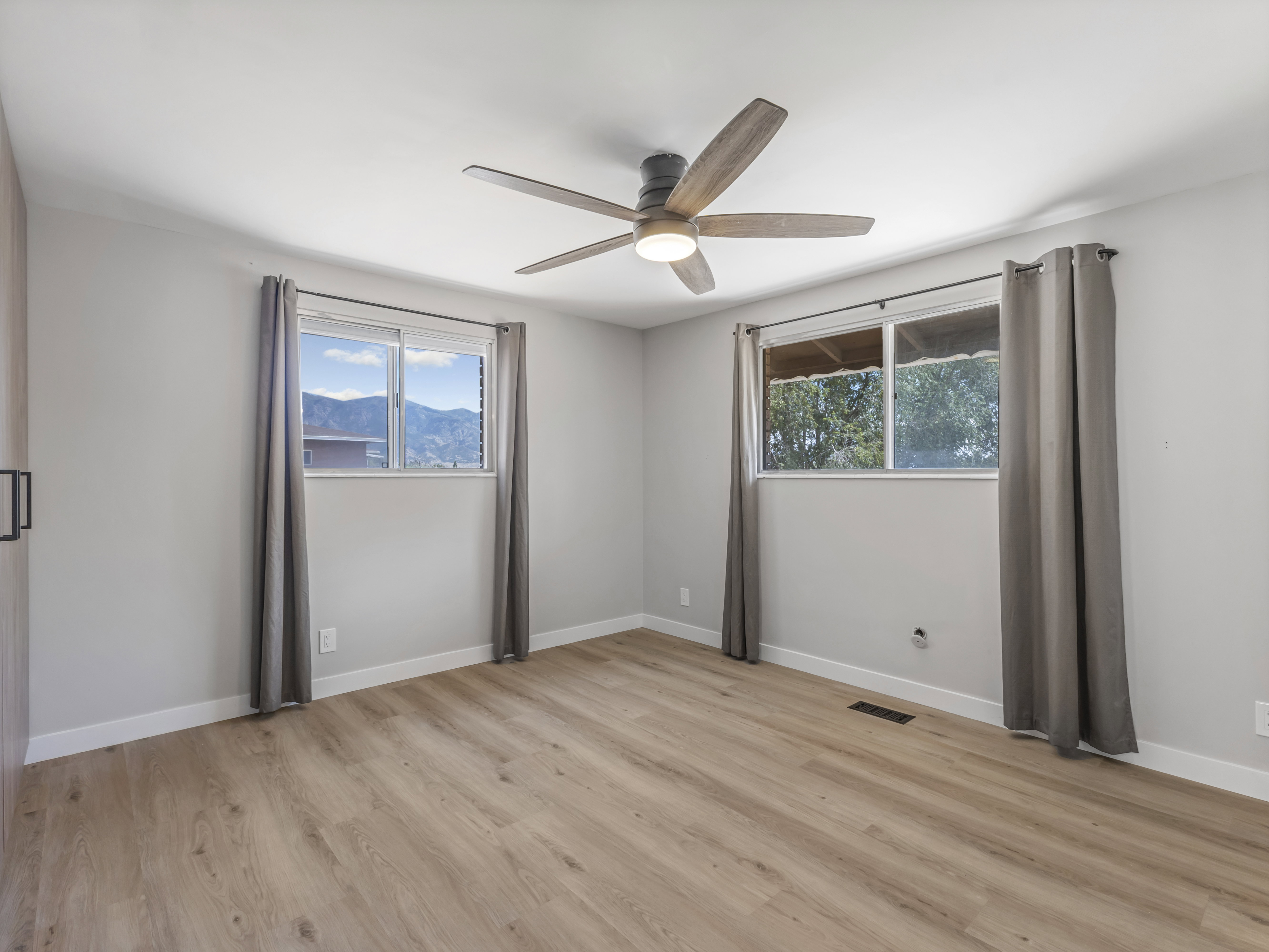 Spacious room featuring wood-finish flooring, two windows with mountain scenery, and a ceiling fan with integrated lighting