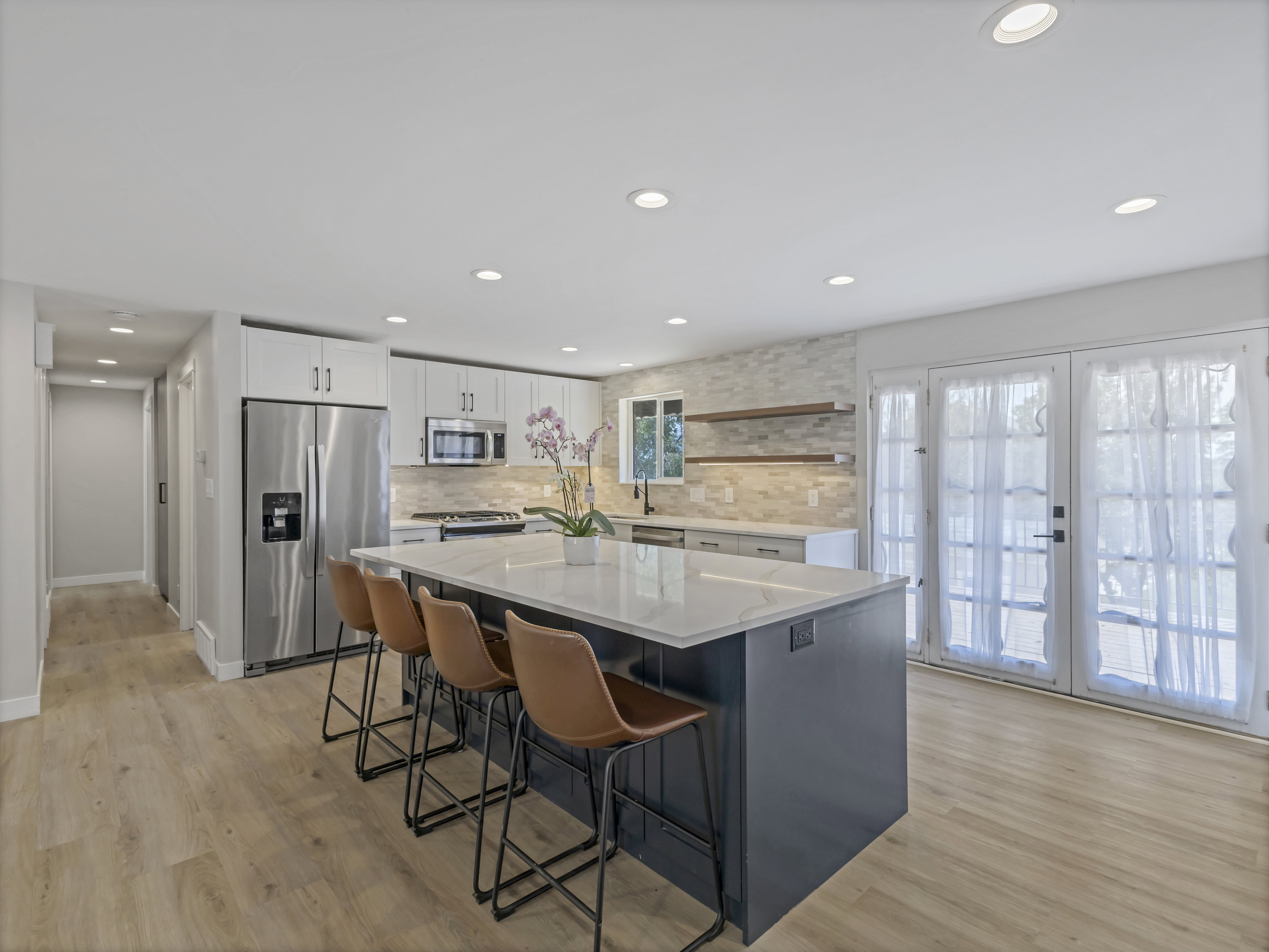 Modern kitchen featuring a large island with seating, stainless steel appliances, light wood-finish flooring, white cabinetry, and a light-toned tile backsplash