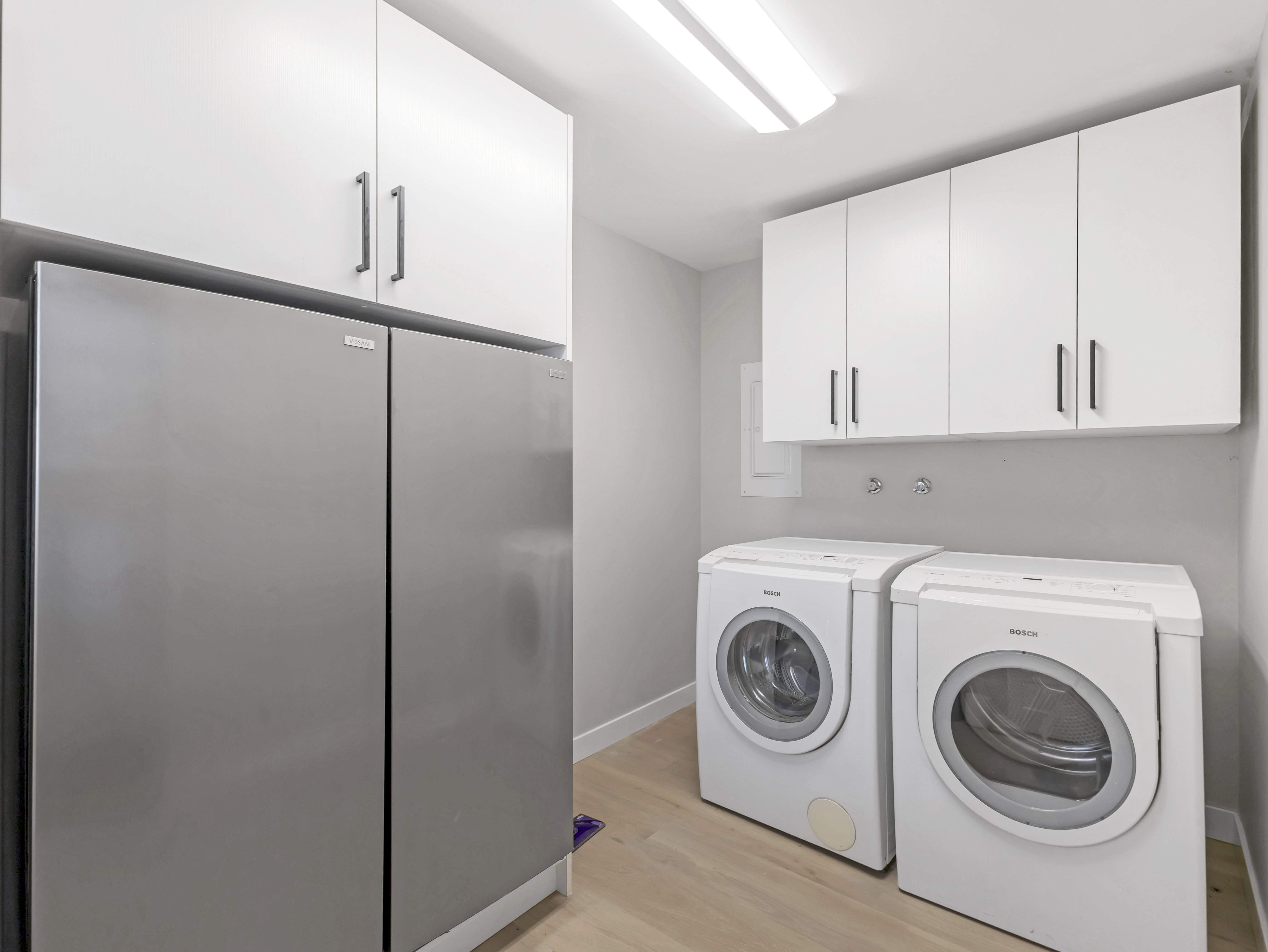 Utility area featuring a side-by-side refrigerator, white cabinetry with contemporary hardware, and wood-finish flooring