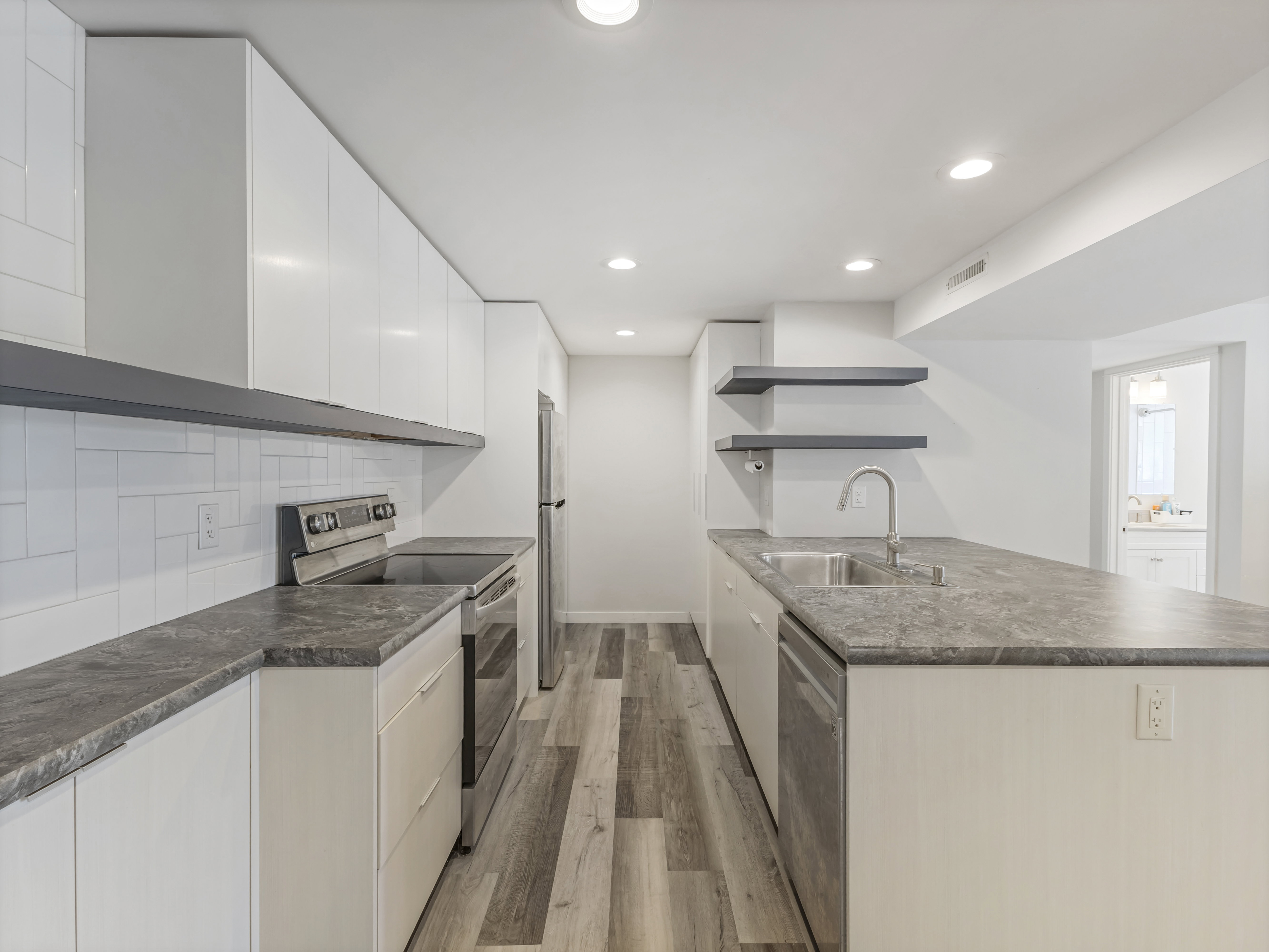 Modern kitchen featuring white flat-panel cabinetry, a stainless steel appliance suite, and wood-finish flooring