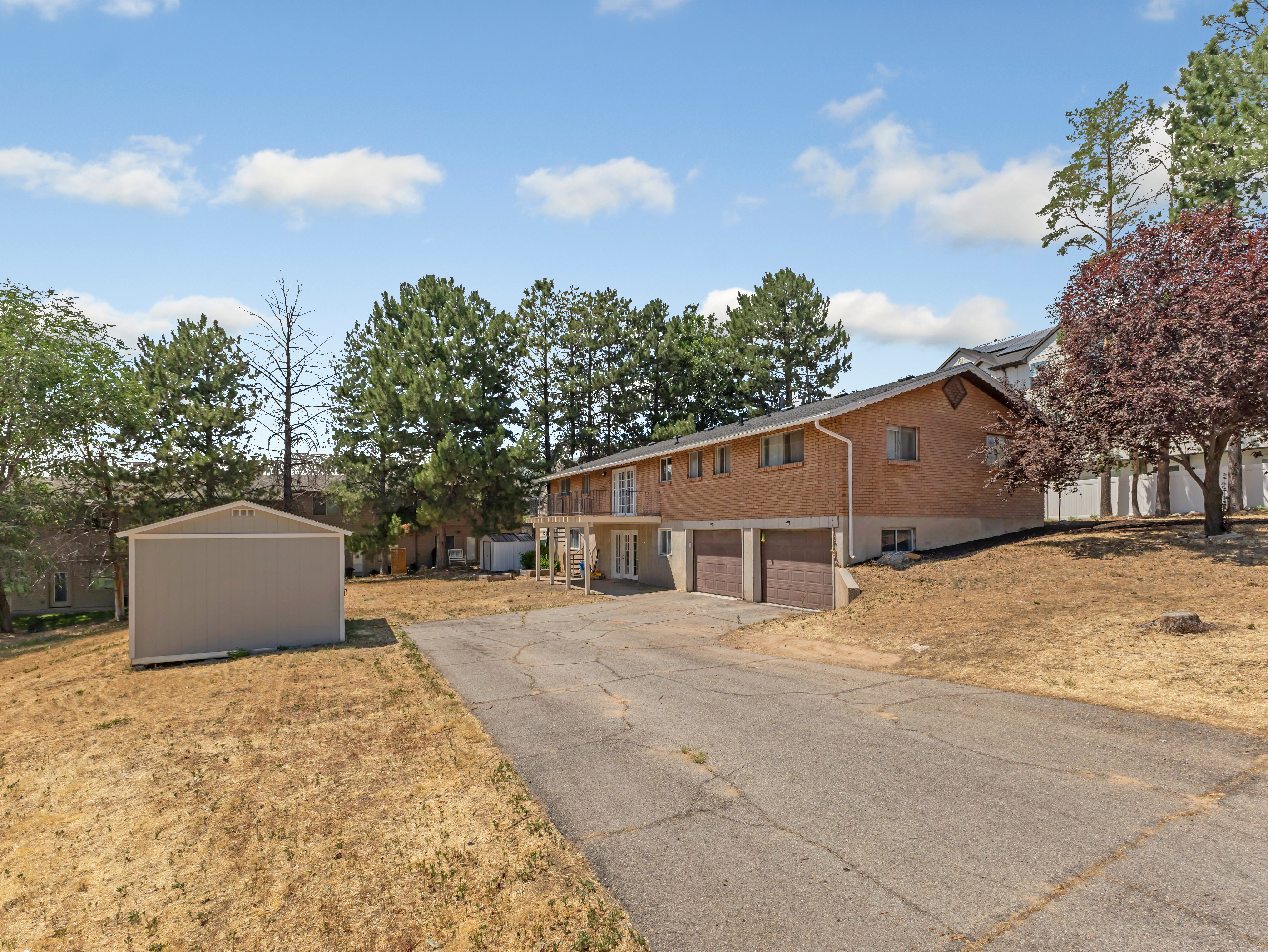 Brick exterior home featuring a concrete driveway, two car garage, upper-level balcony, and a separate storage shed