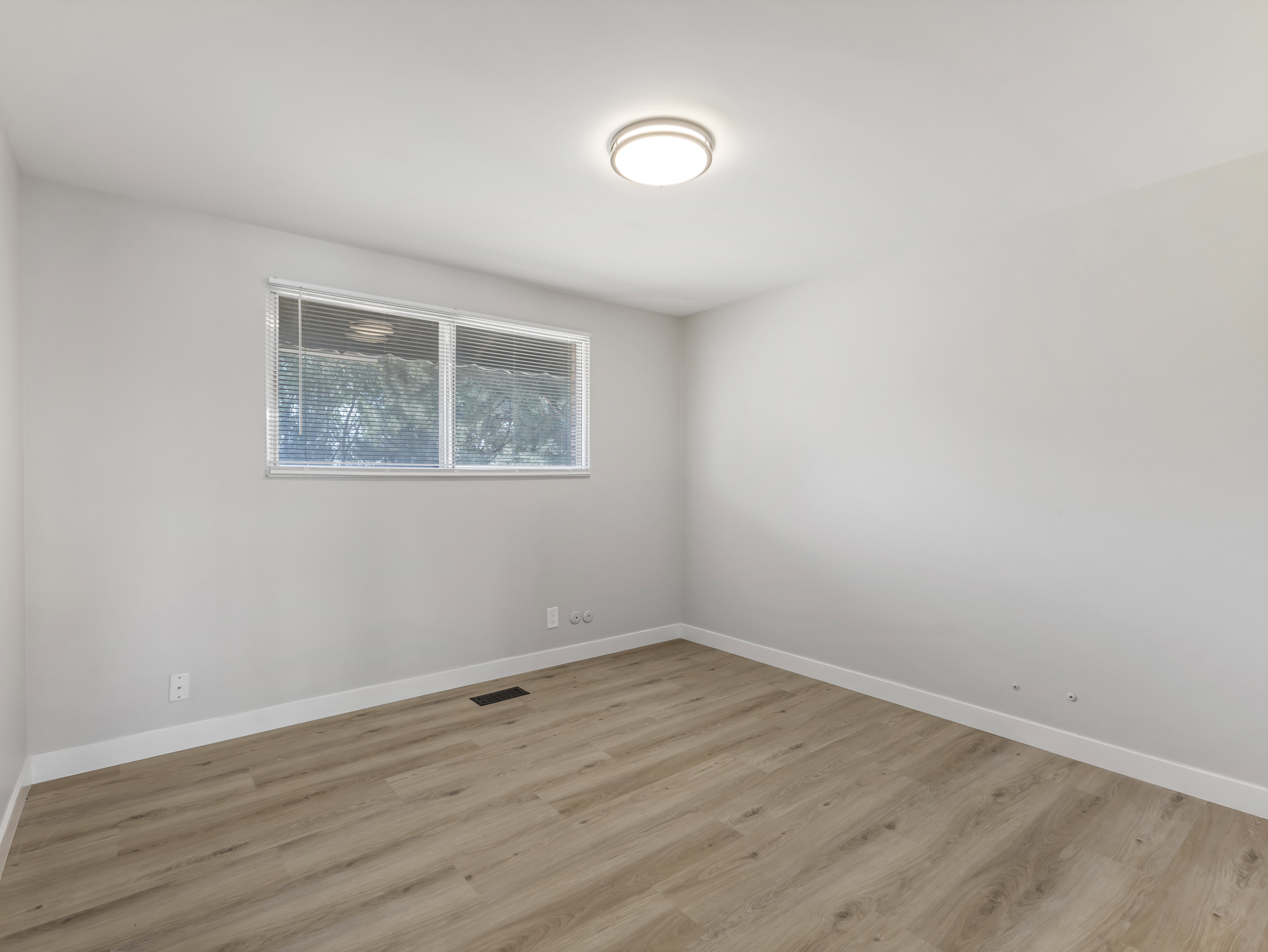Bright interior space featuring light wood-finish flooring, a contemporary flush-mount ceiling light, white baseboards, and a double-pane window with blinds