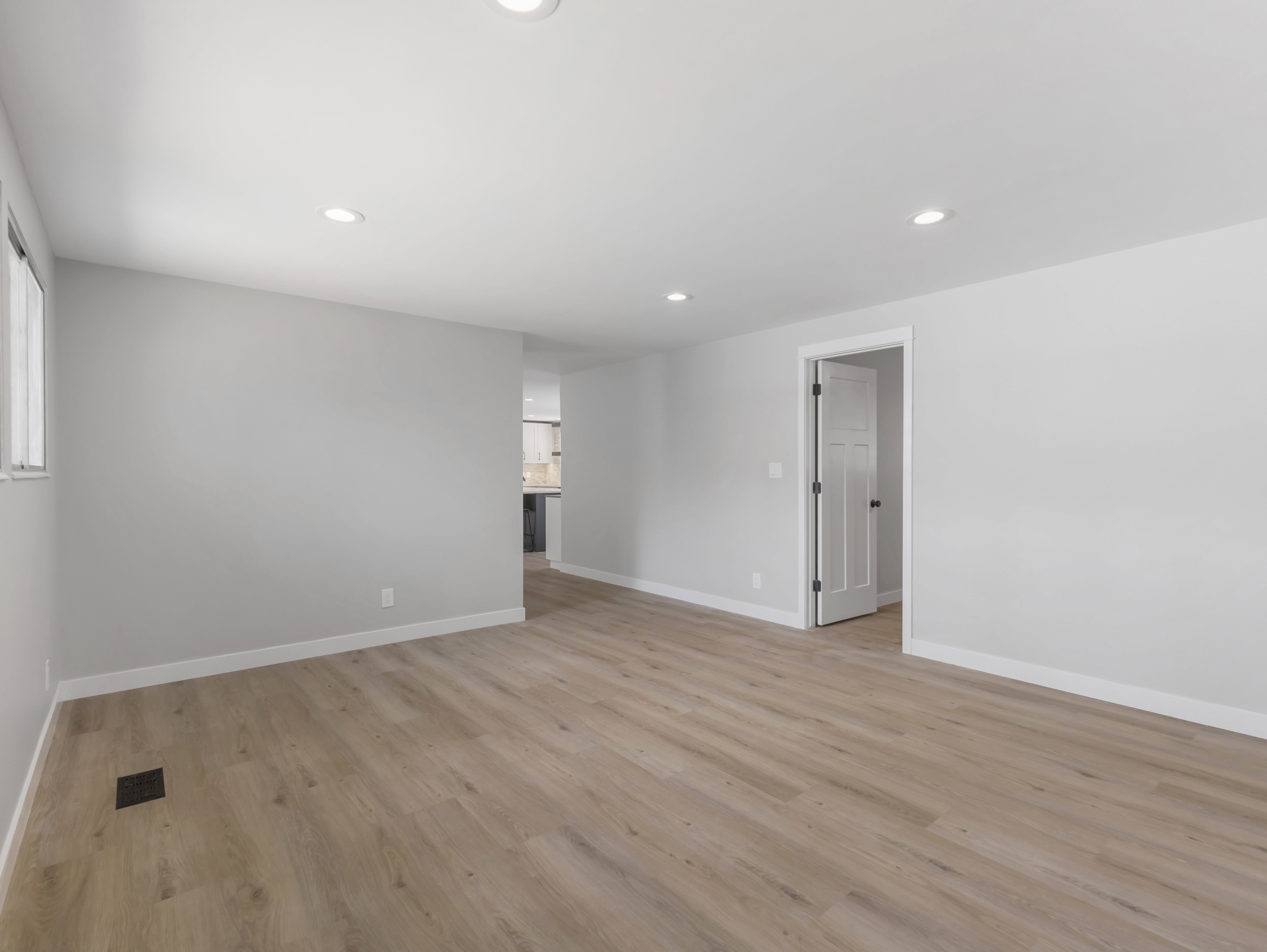 Spacious room featuring wood-finish flooring, light grey walls, white baseboards, recessed lighting, and a window for natural illumination