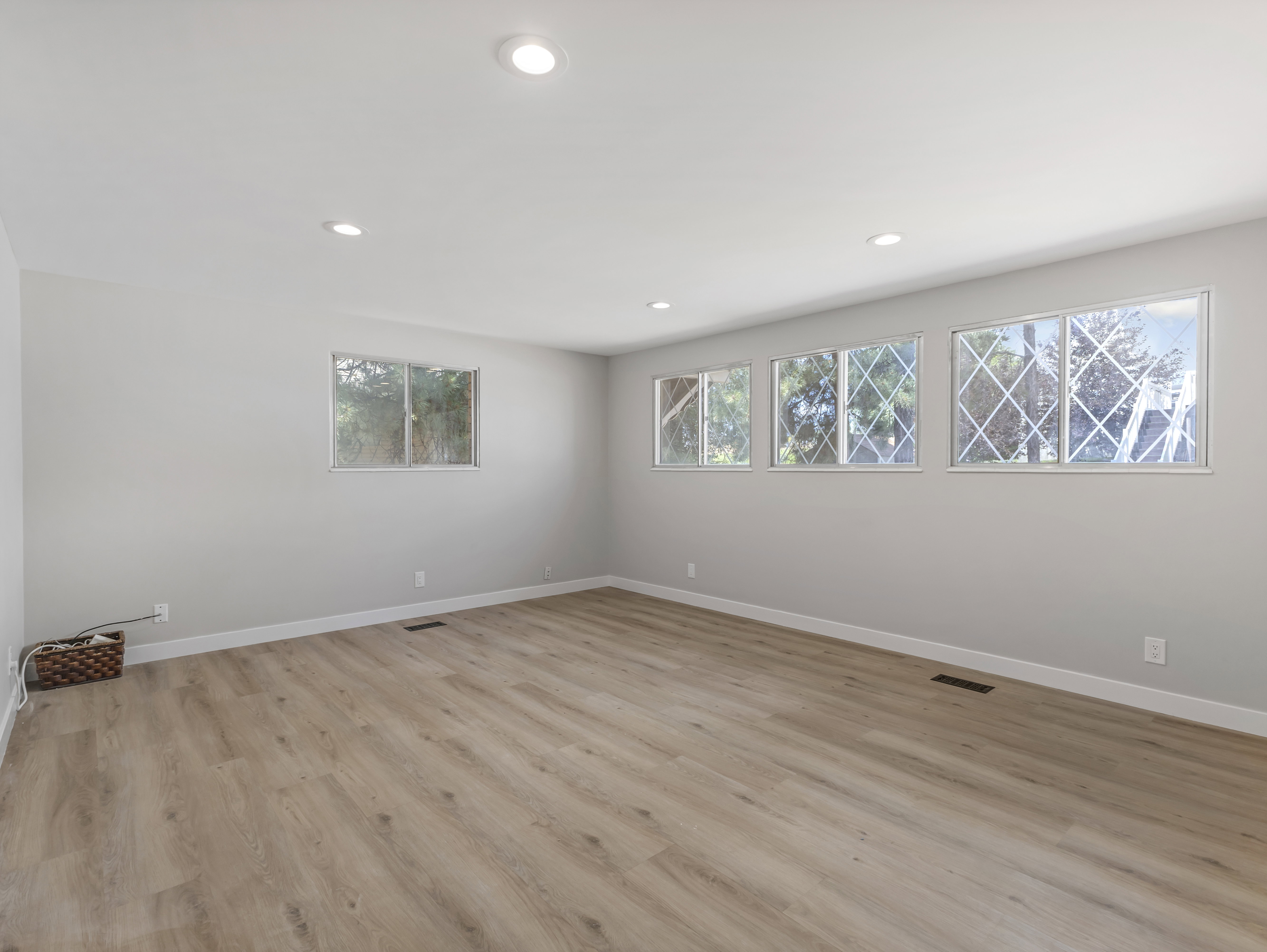 Spacious room featuring light wood-finish flooring, recessed lighting, multiple windows, and crisp white baseboards