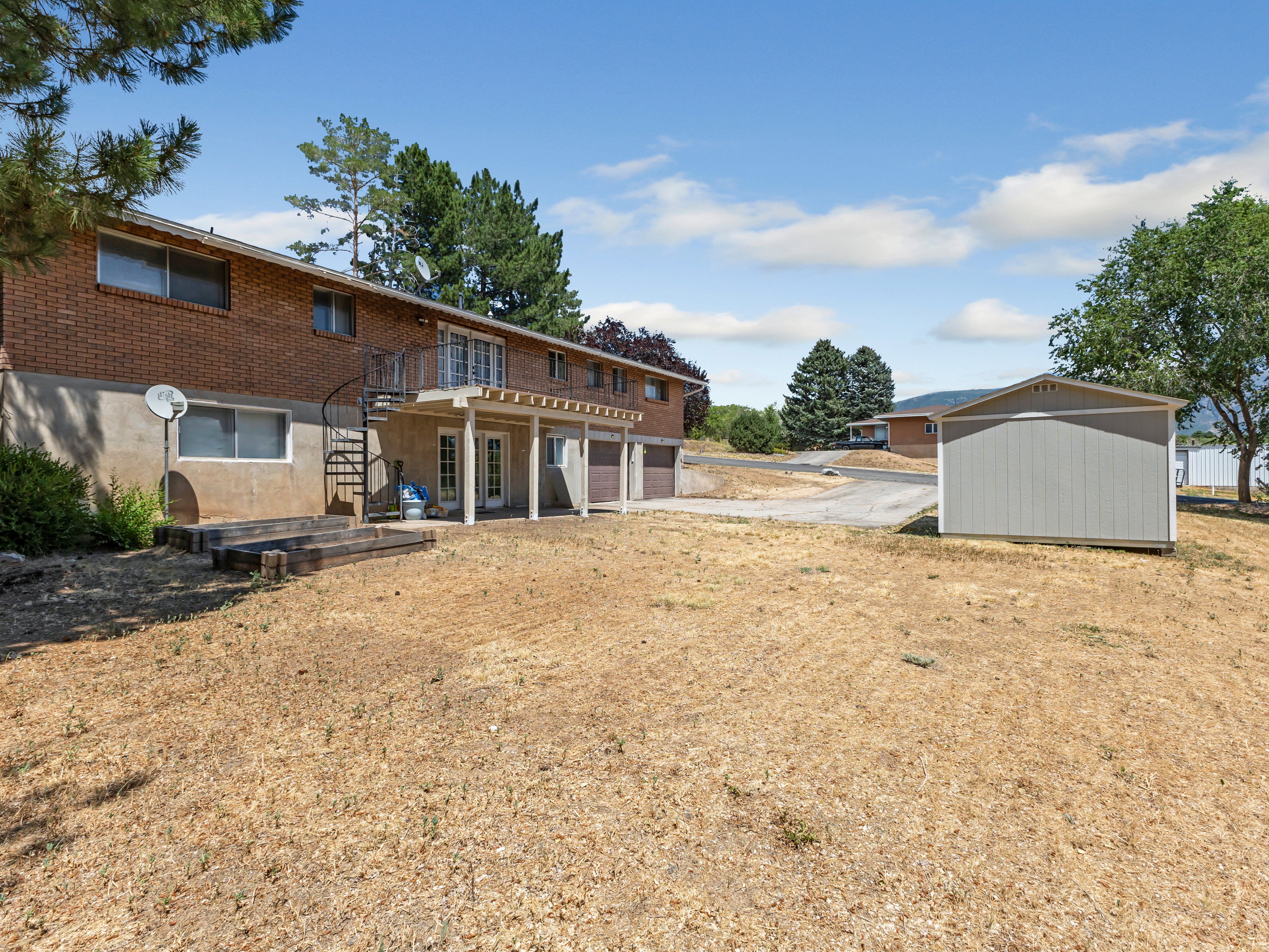 Expansive rear yard with a detached storage shed, offering a brick exterior, a covered patio, and a spiral staircase leading to an upper-level balcony