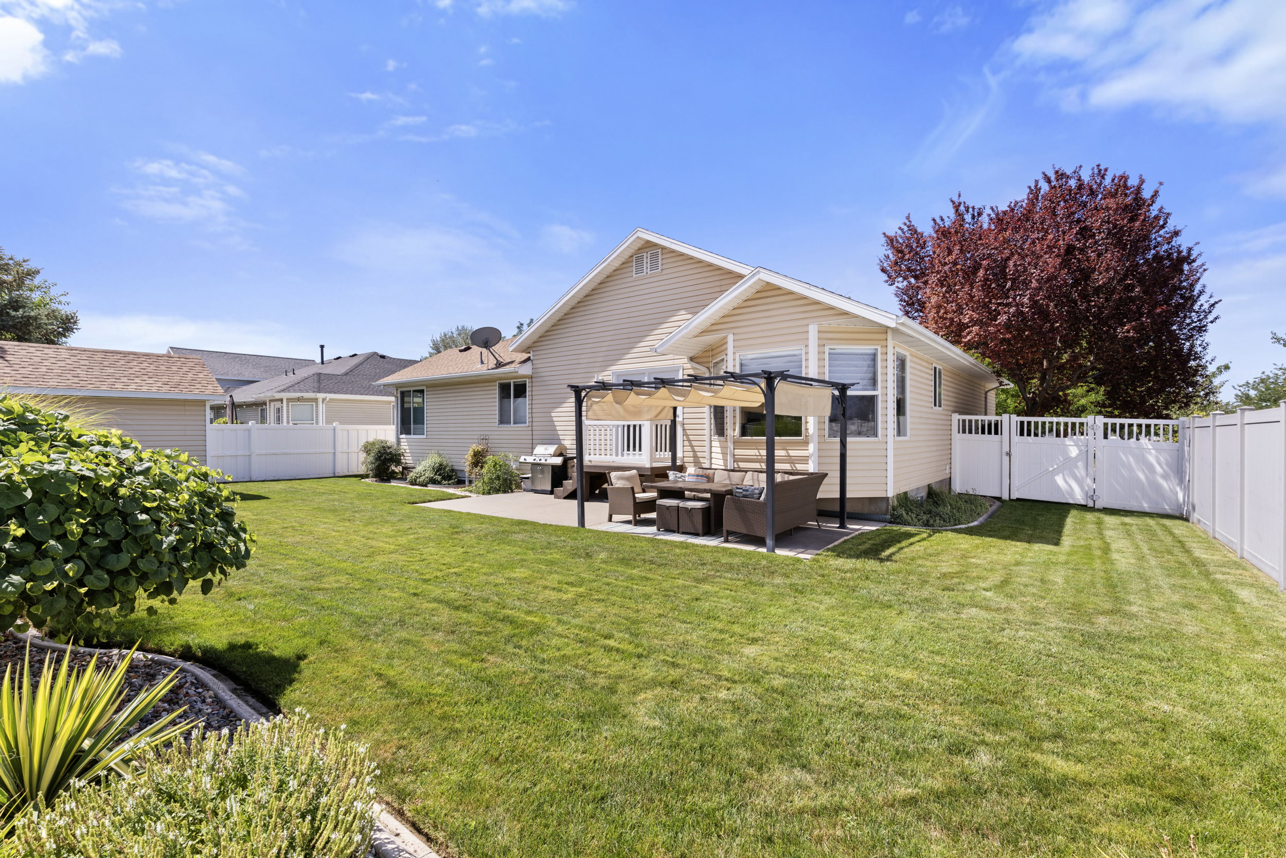 Expansive backyard featuring a large concrete patio, a pergola-covered outdoor dining area, a substantial lawn, and white privacy fencing