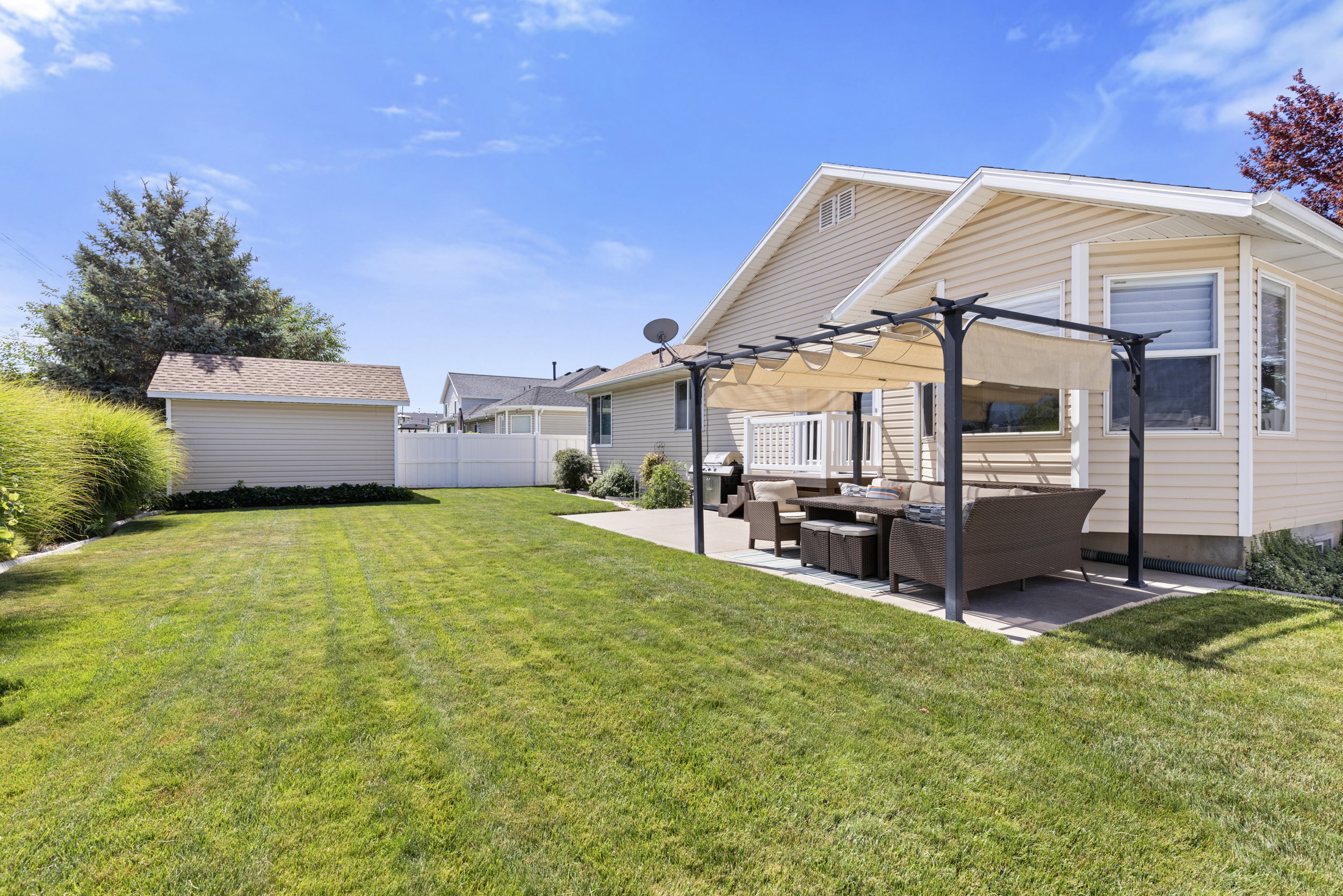 Expansive backyard featuring a concrete patio with a pergola, a detached storage shed, and mature green landscaping