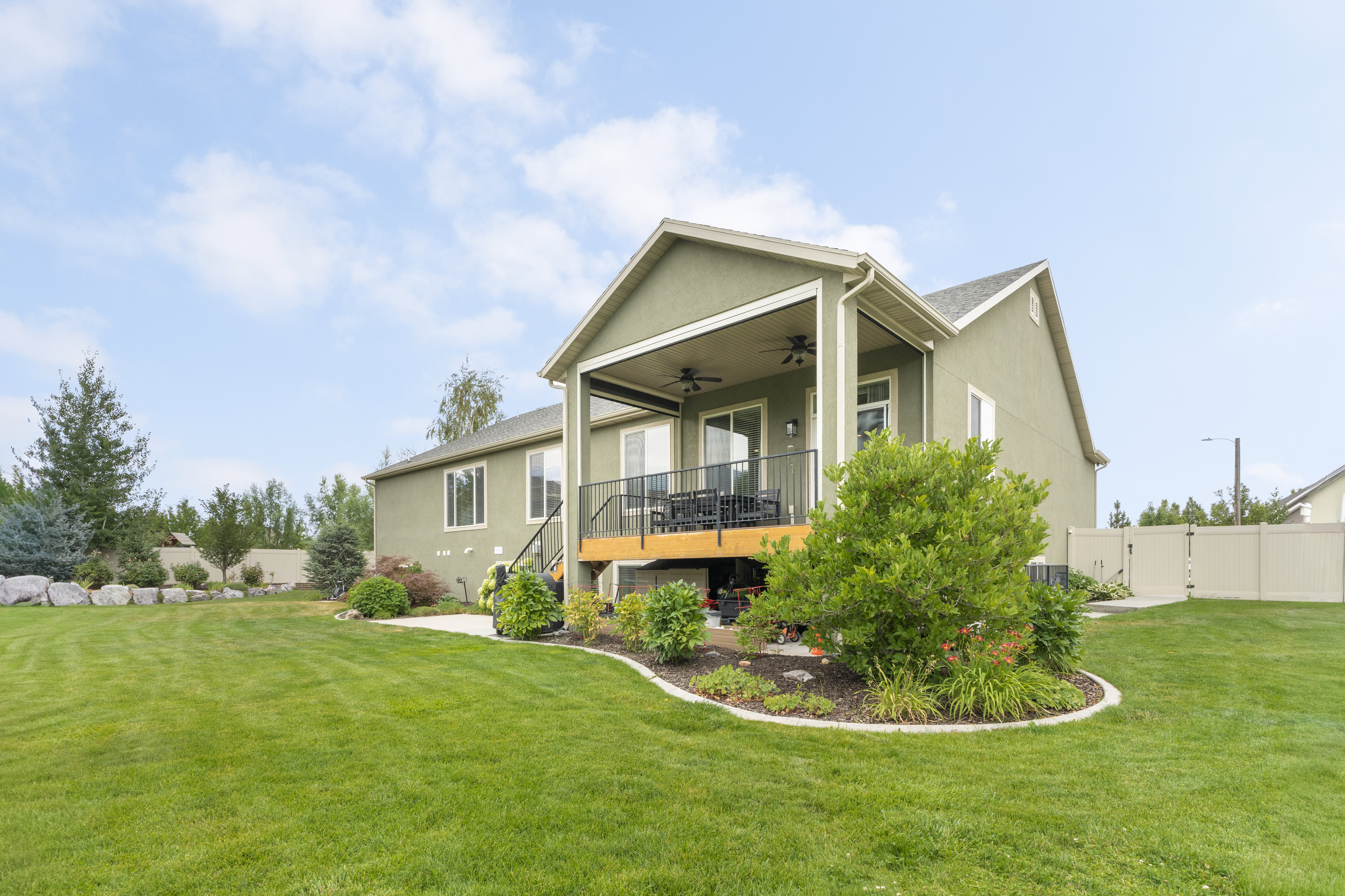 Expansive rear yard featuring a covered deck with ceiling fans, a lower concrete patio, and a perimeter of mature landscaping