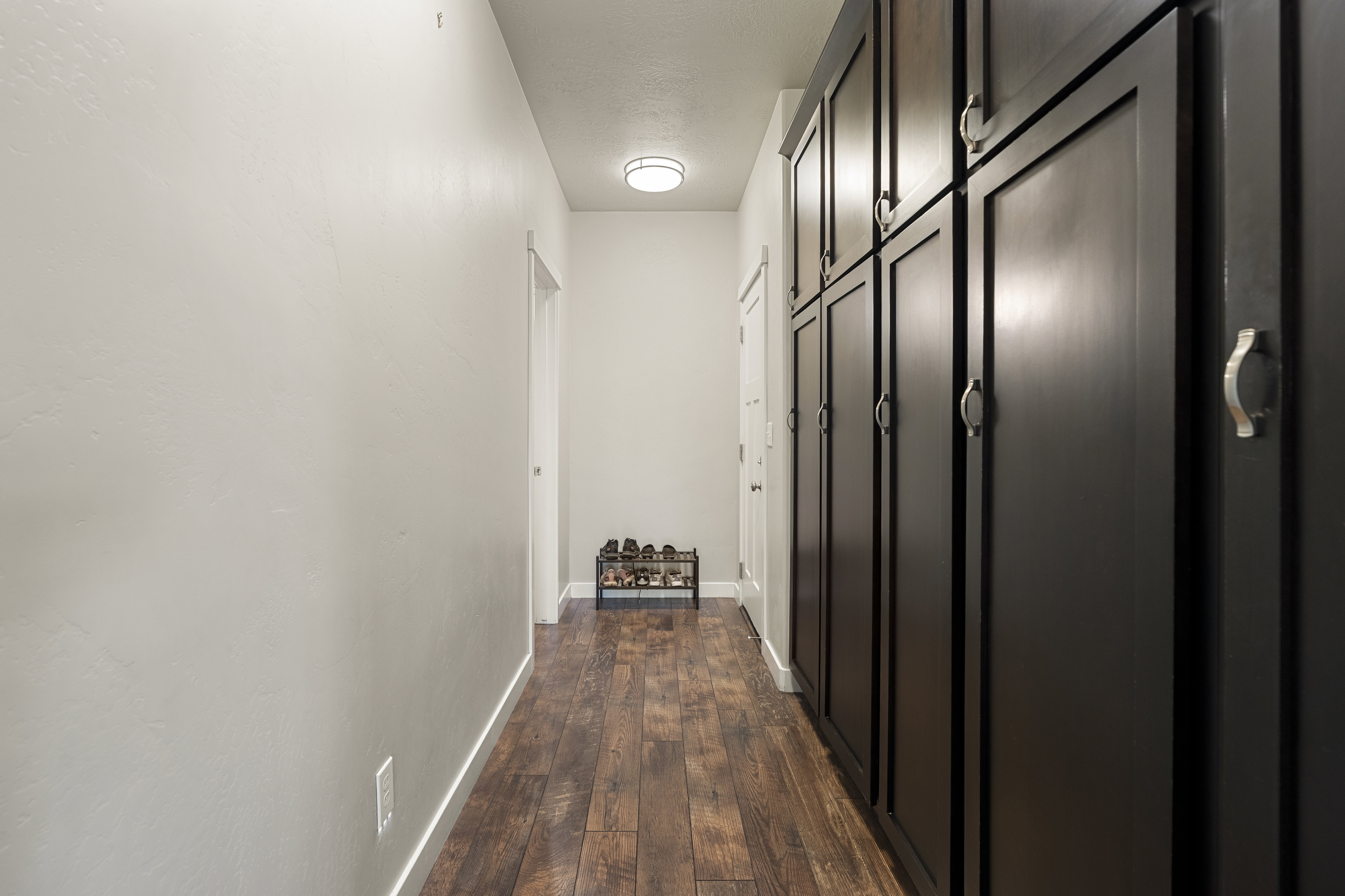 Hallway featuring extensive dark wood cabinetry, wood-finish flooring, and white baseboards