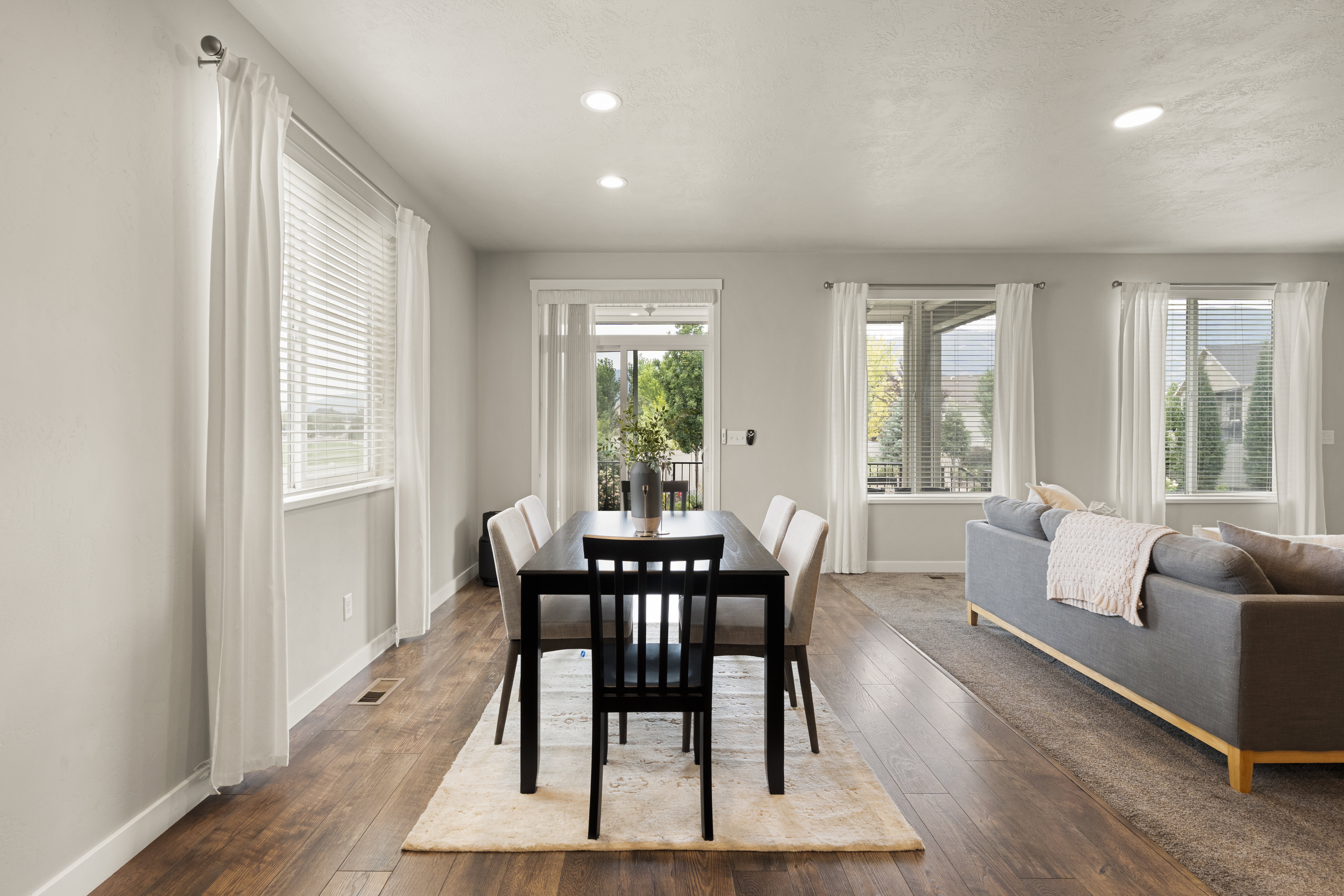 Open-concept living area featuring wood-finish flooring, recessed lighting, multiple windows with blinds, and white trim