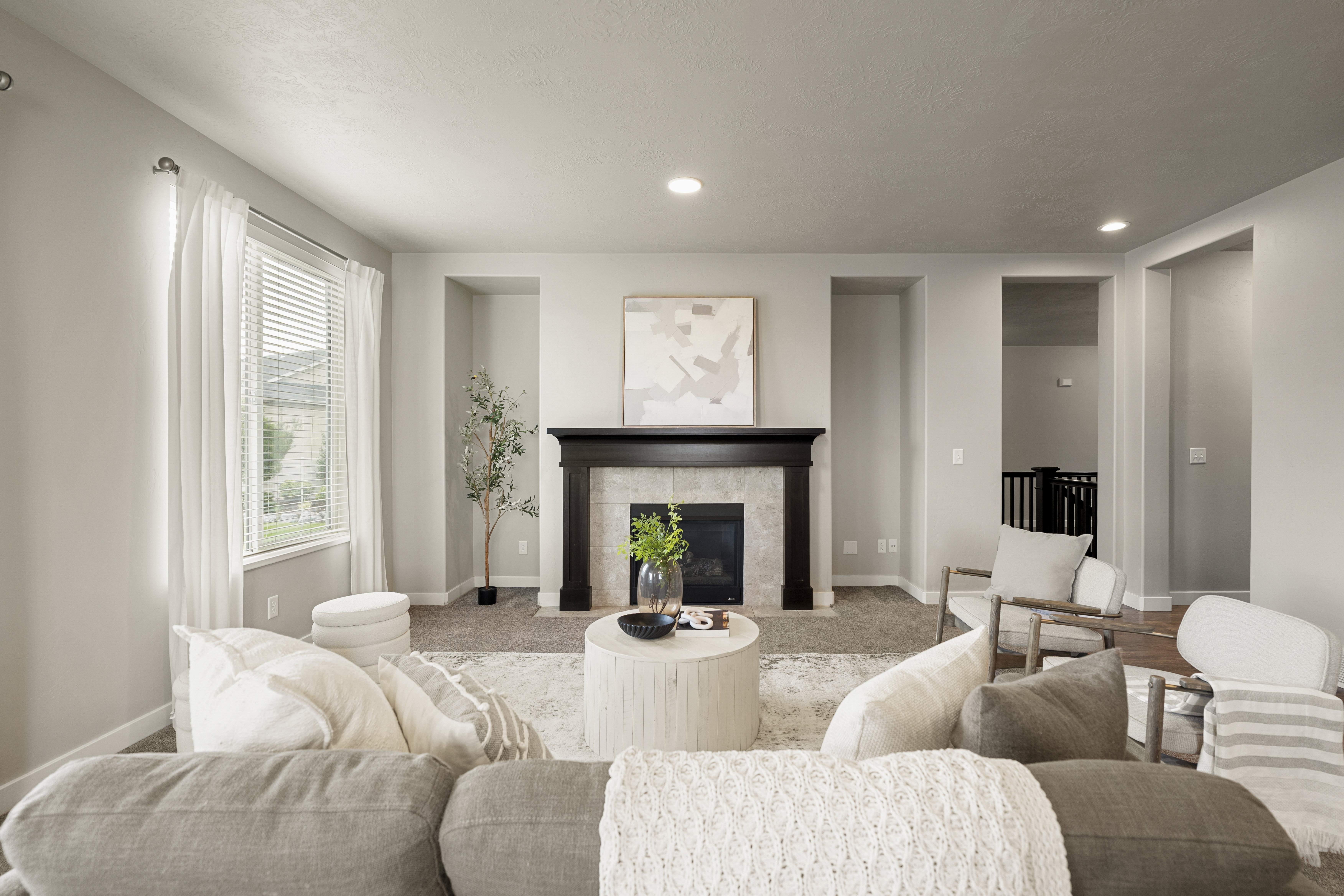 Spacious living area featuring a decorative fireplace with a dark wood mantel and light-toned surround, recessed lighting, and a large window with horizontal blinds