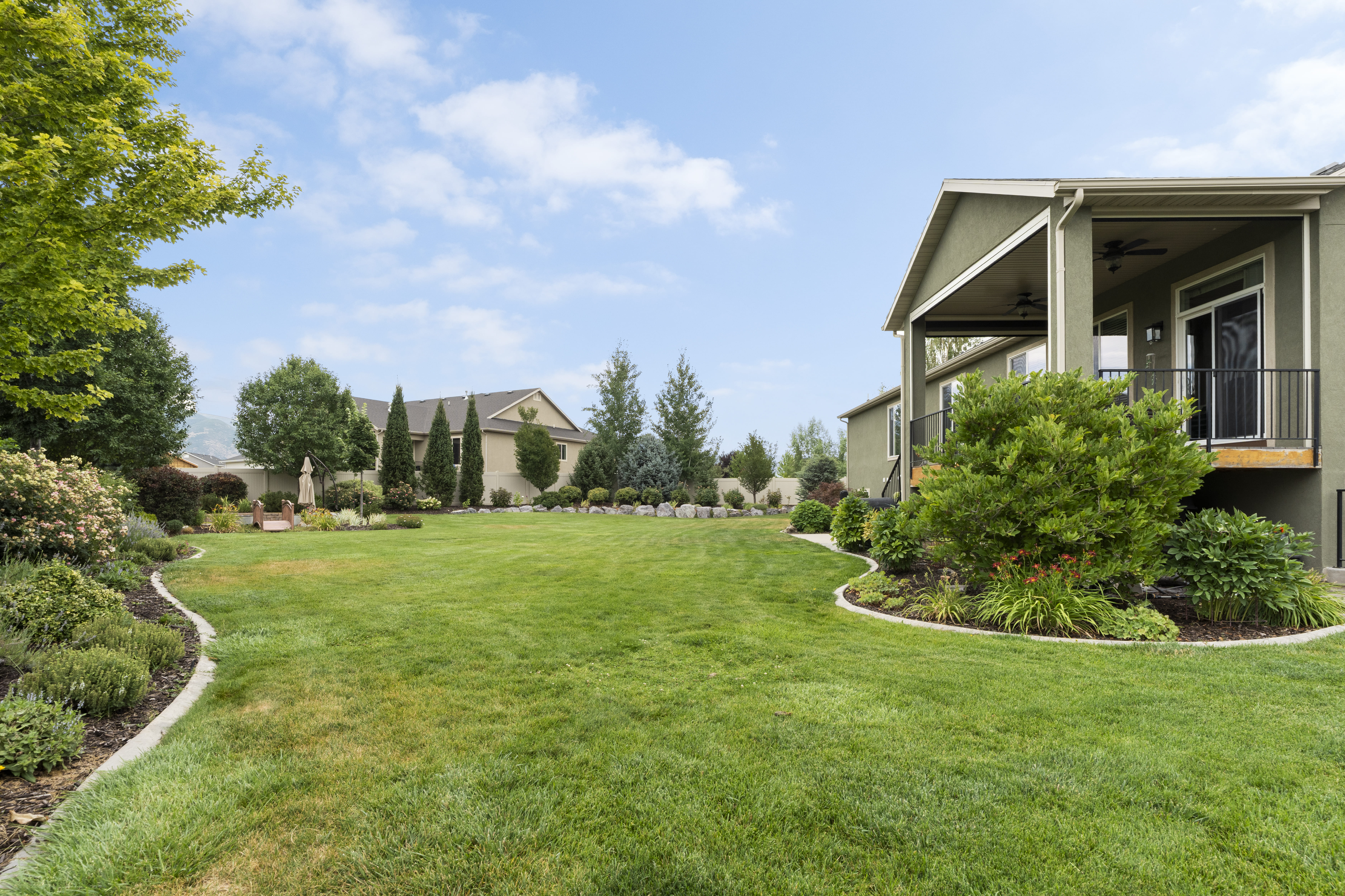 Expansive backyard featuring a lush lawn, mature trees, and landscaped garden beds with concrete curbing