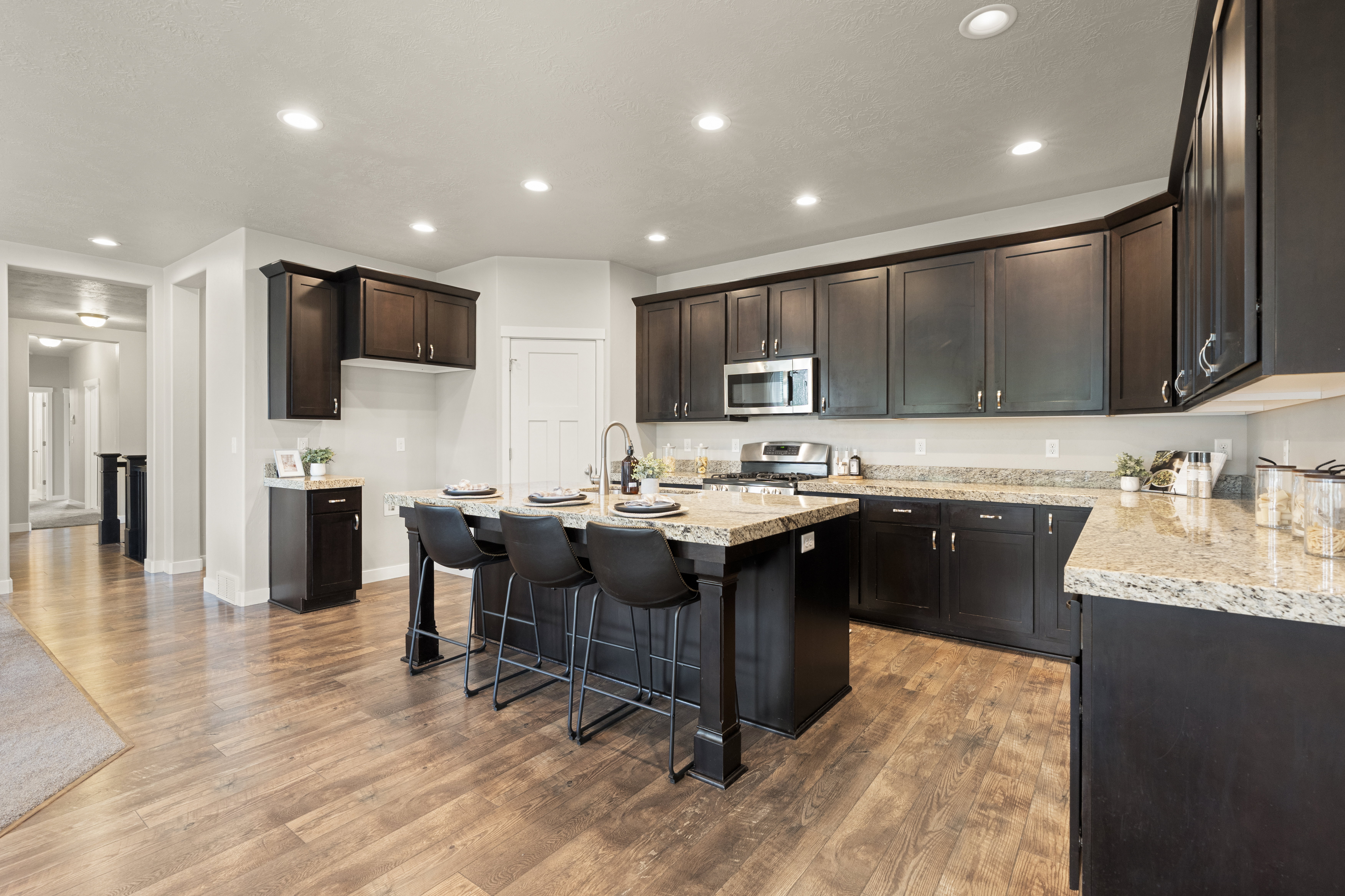 Spacious kitchen featuring an island with seating, granite countertops, wood-finish flooring, dark wood cabinetry, and recessed lighting