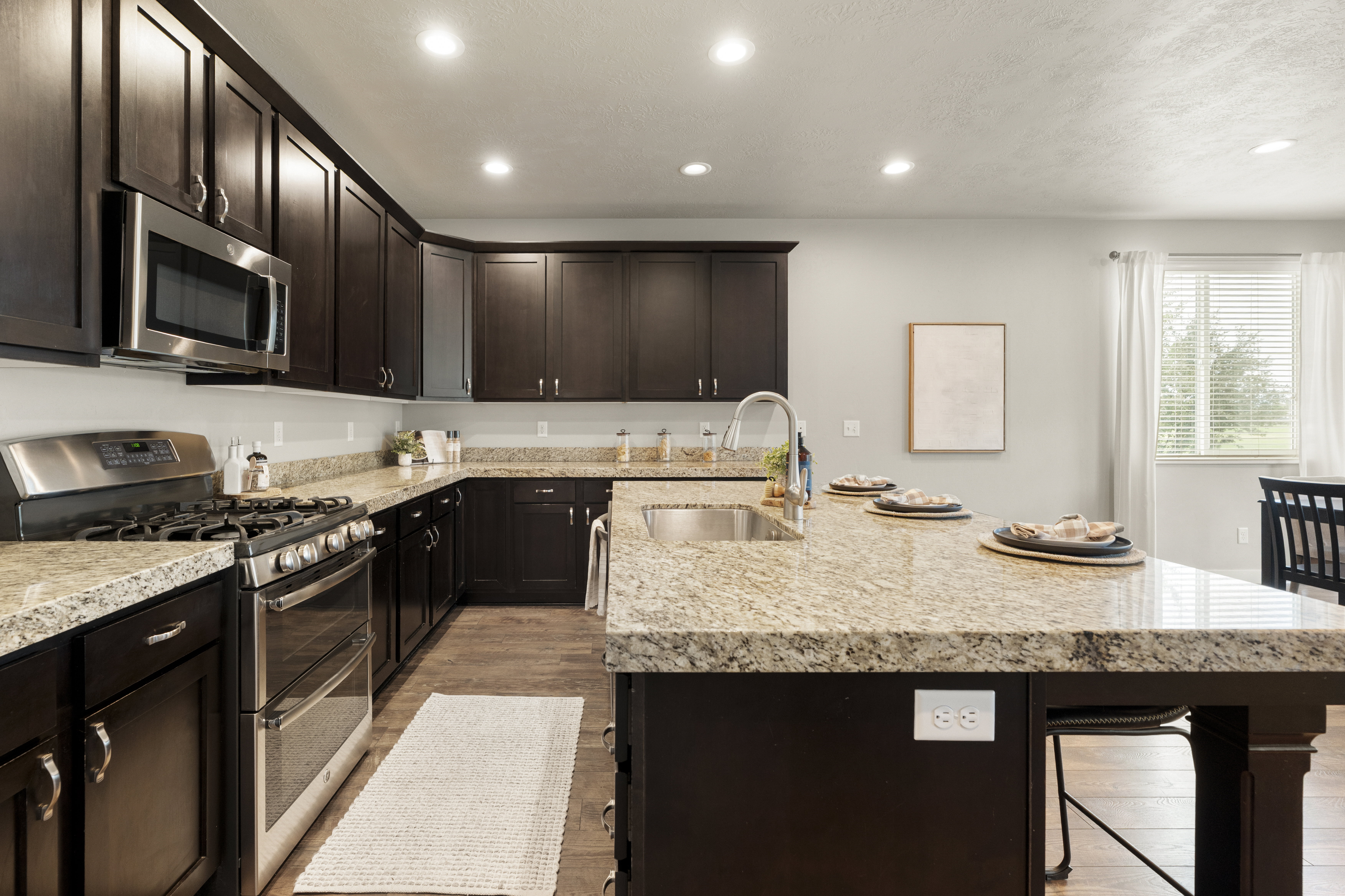 Kitchen featuring dark wood cabinetry, light speckled countertops, stainless steel appliances, wood-finish flooring, and recessed lighting