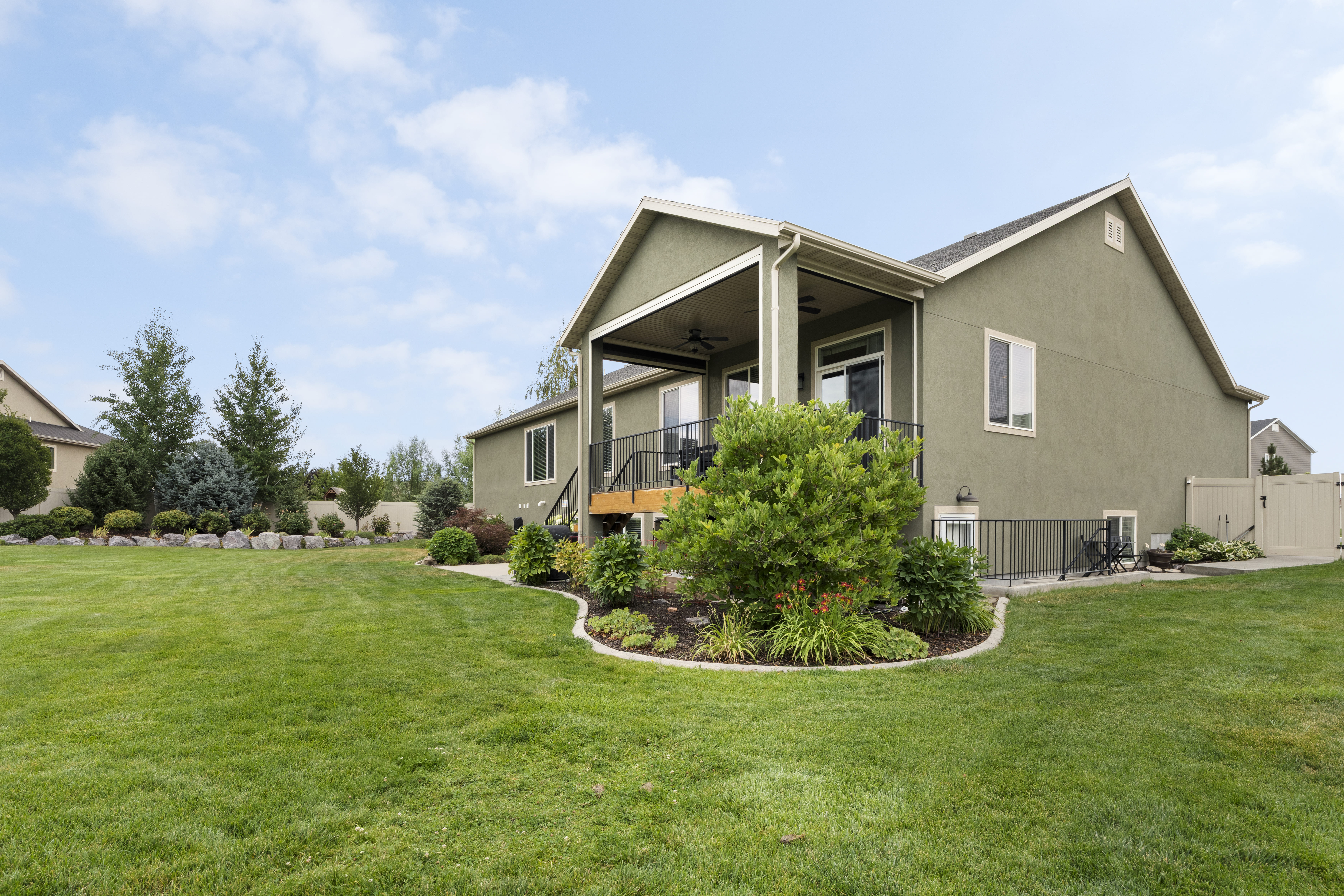 Expansive green lawn with a large rear patio, covered balcony, and mature landscaping