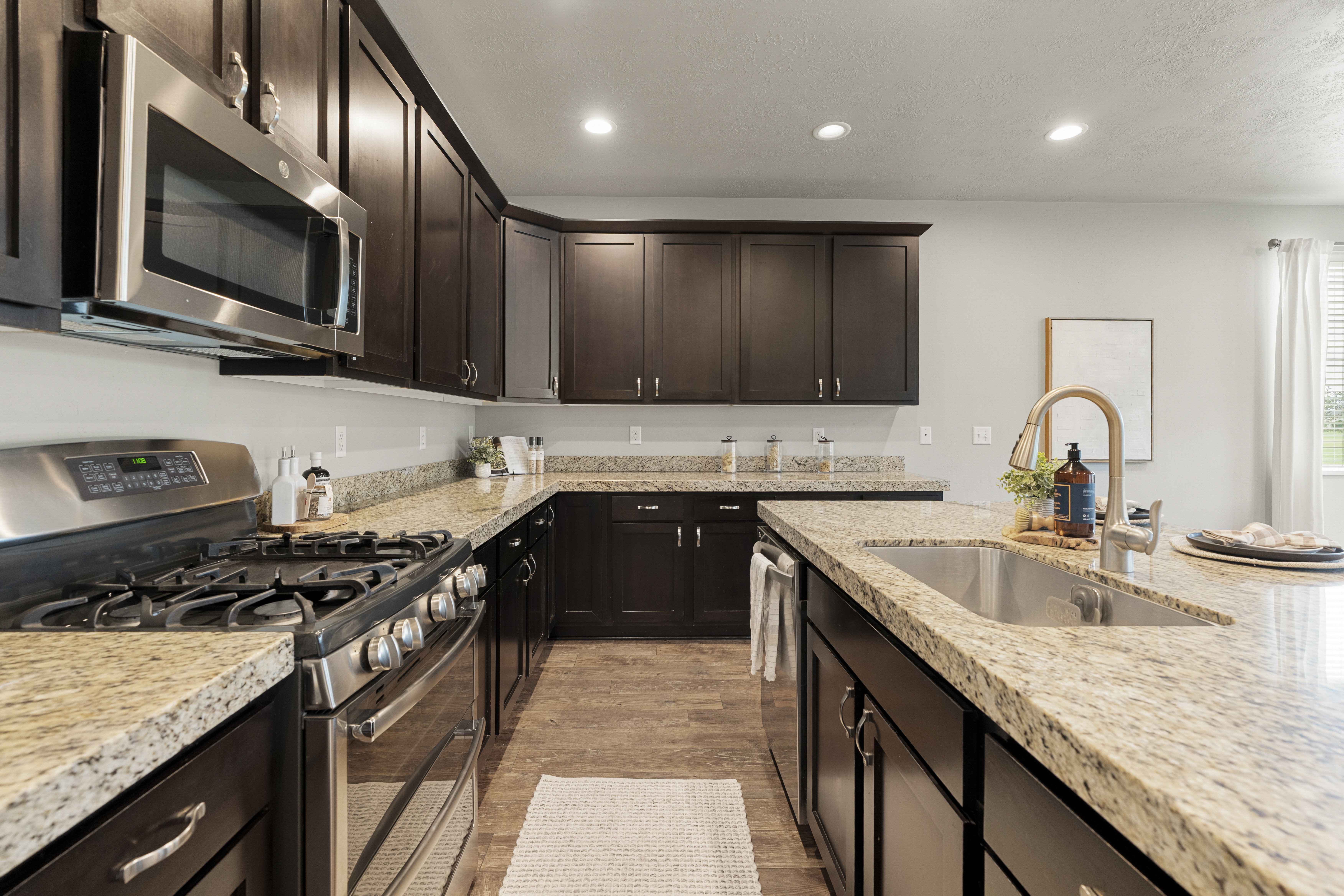 Kitchen featuring dark wood cabinetry, light granite countertops, stainless steel appliances, a gas range, and wood-finish flooring