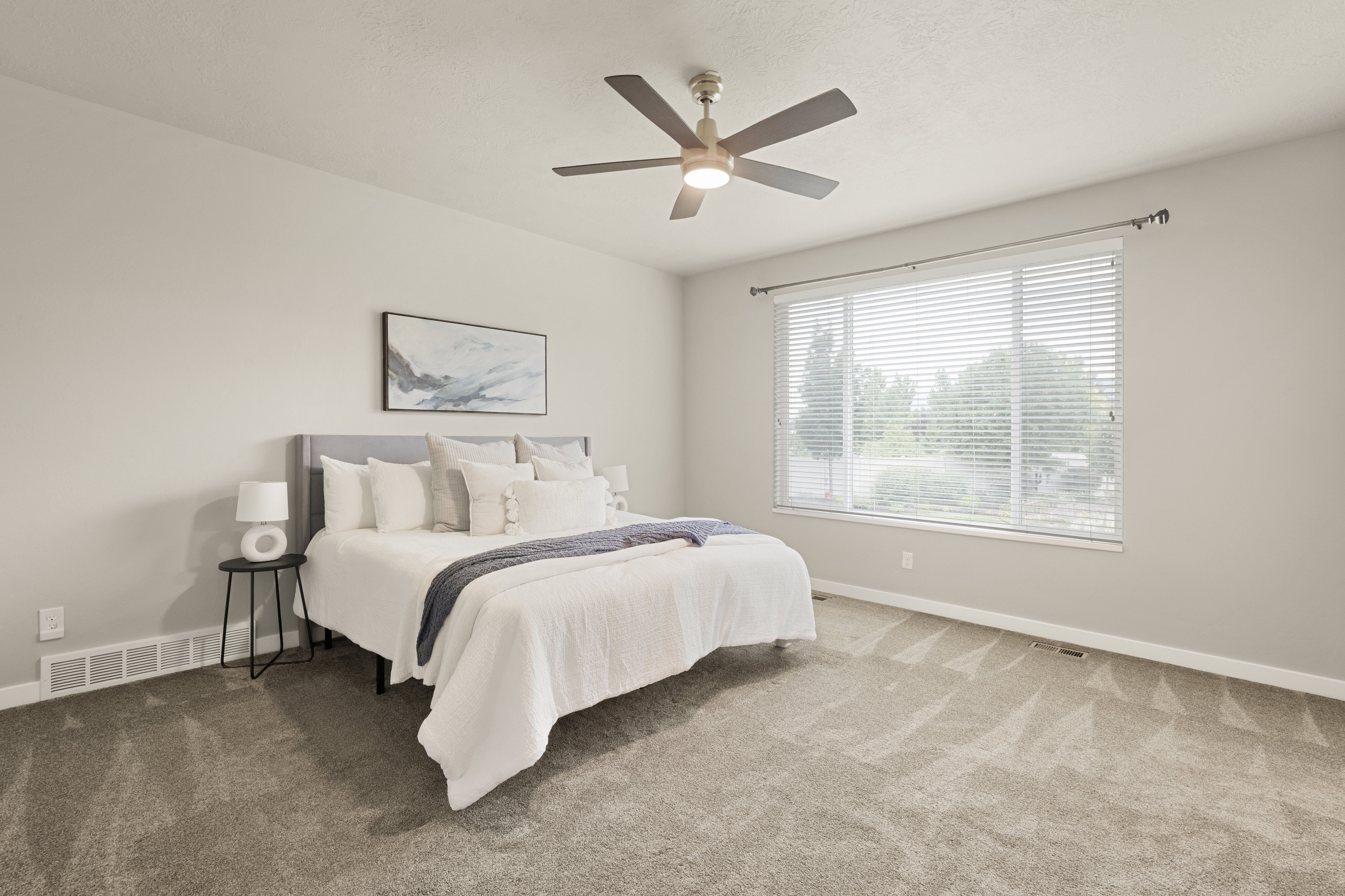 Spacious room featuring neutral carpeting, a large window with horizontal blinds, and a ceiling fan with integrated lighting