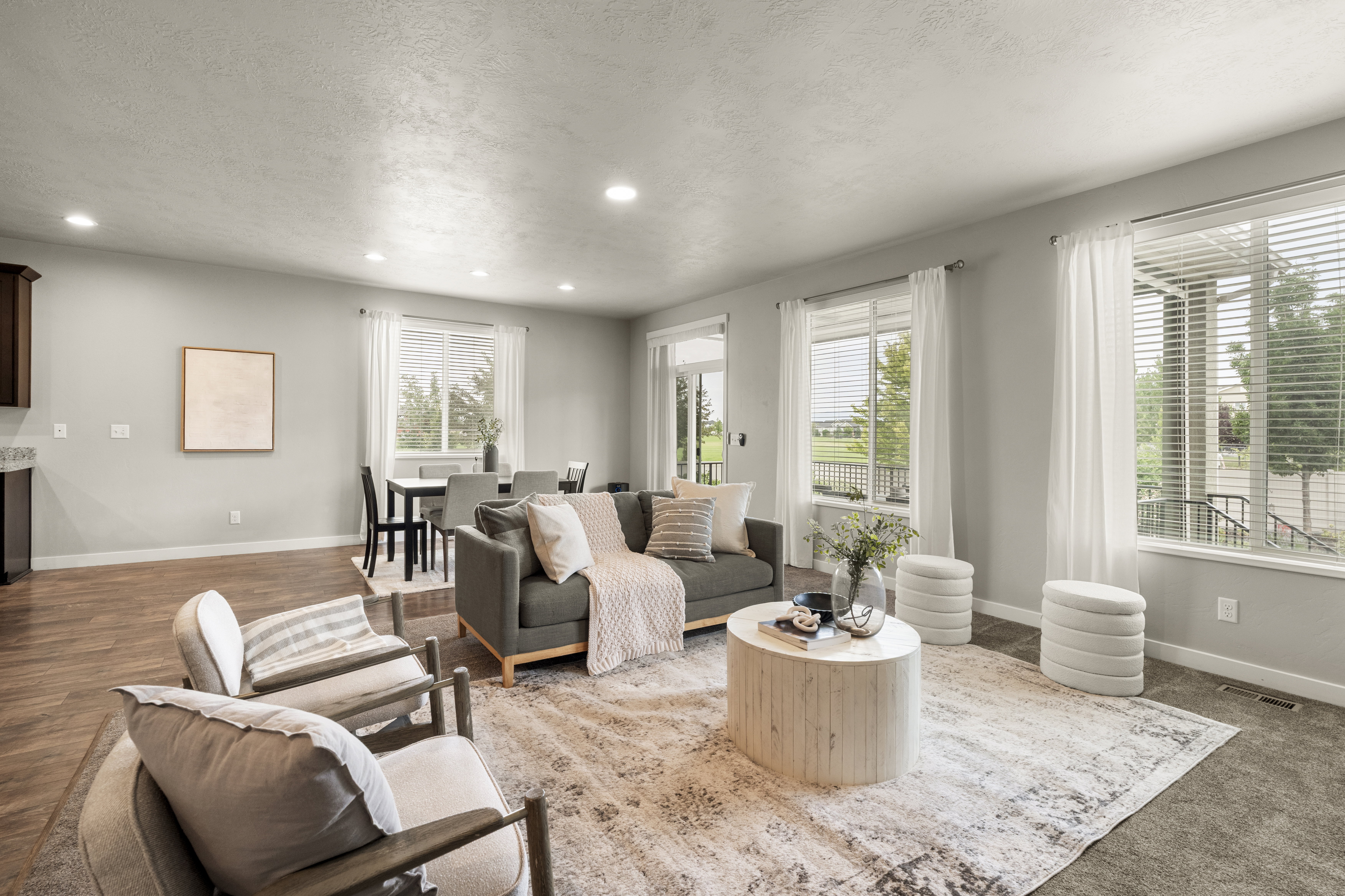Spacious living area featuring light-toned walls, recessed lighting, and a combination of wood-finish flooring and carpet