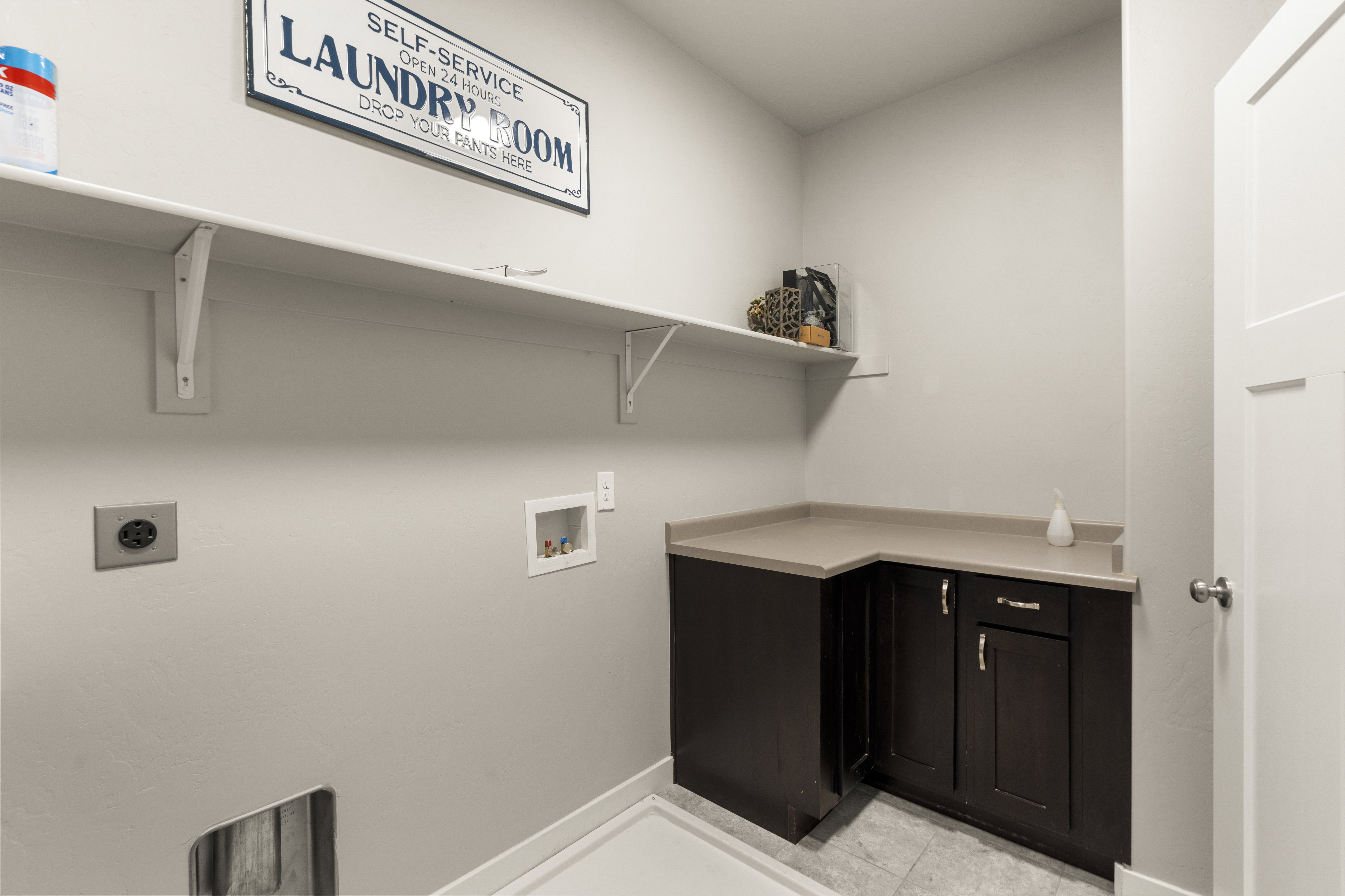 Dedicated laundry area featuring white walls, an upper storage shelf, and dark wood-finish cabinetry with a light-toned countertop