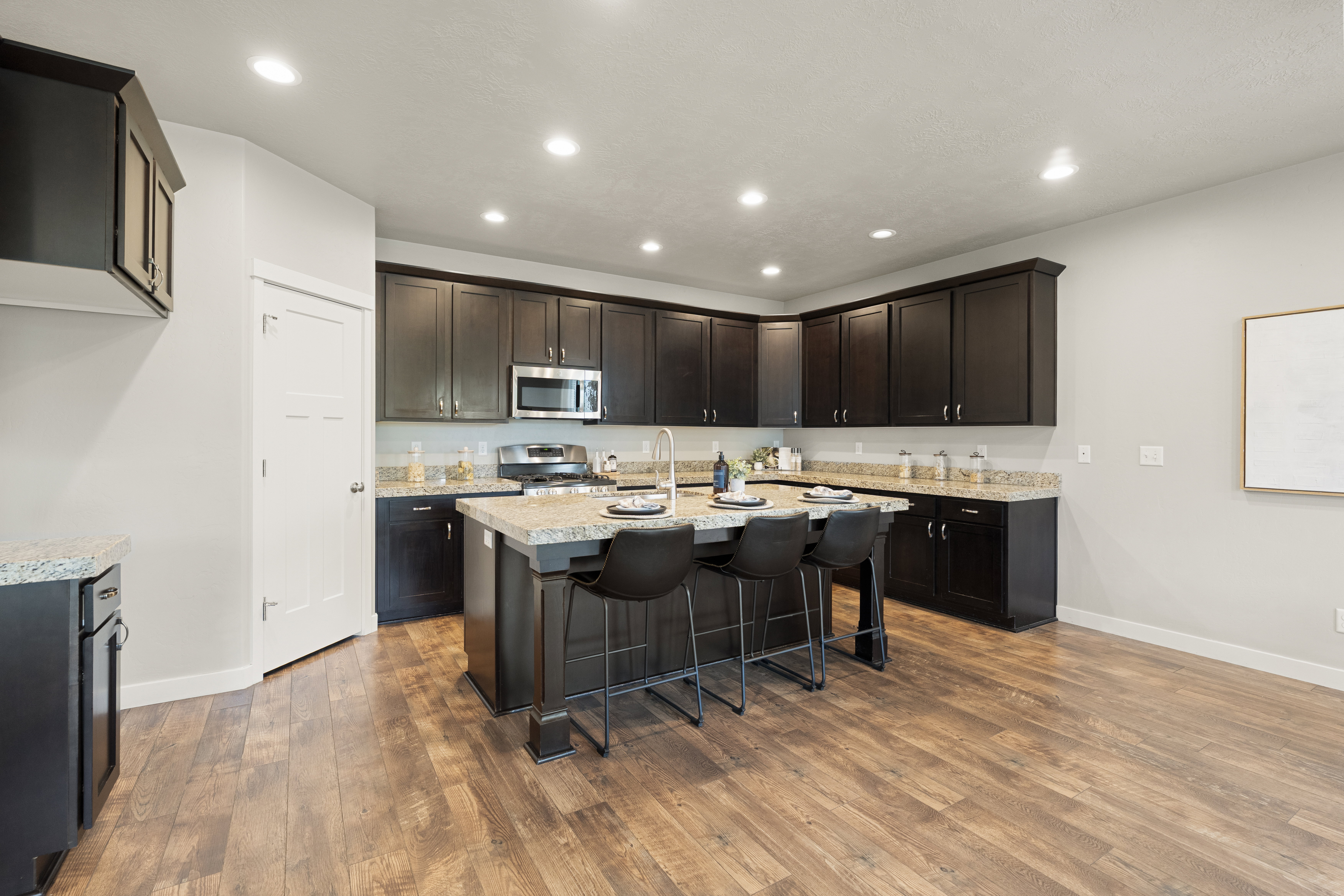 Modern kitchen featuring dark wood cabinetry, granite countertops, stainless steel appliances, a center island with seating, and wood-finish flooring