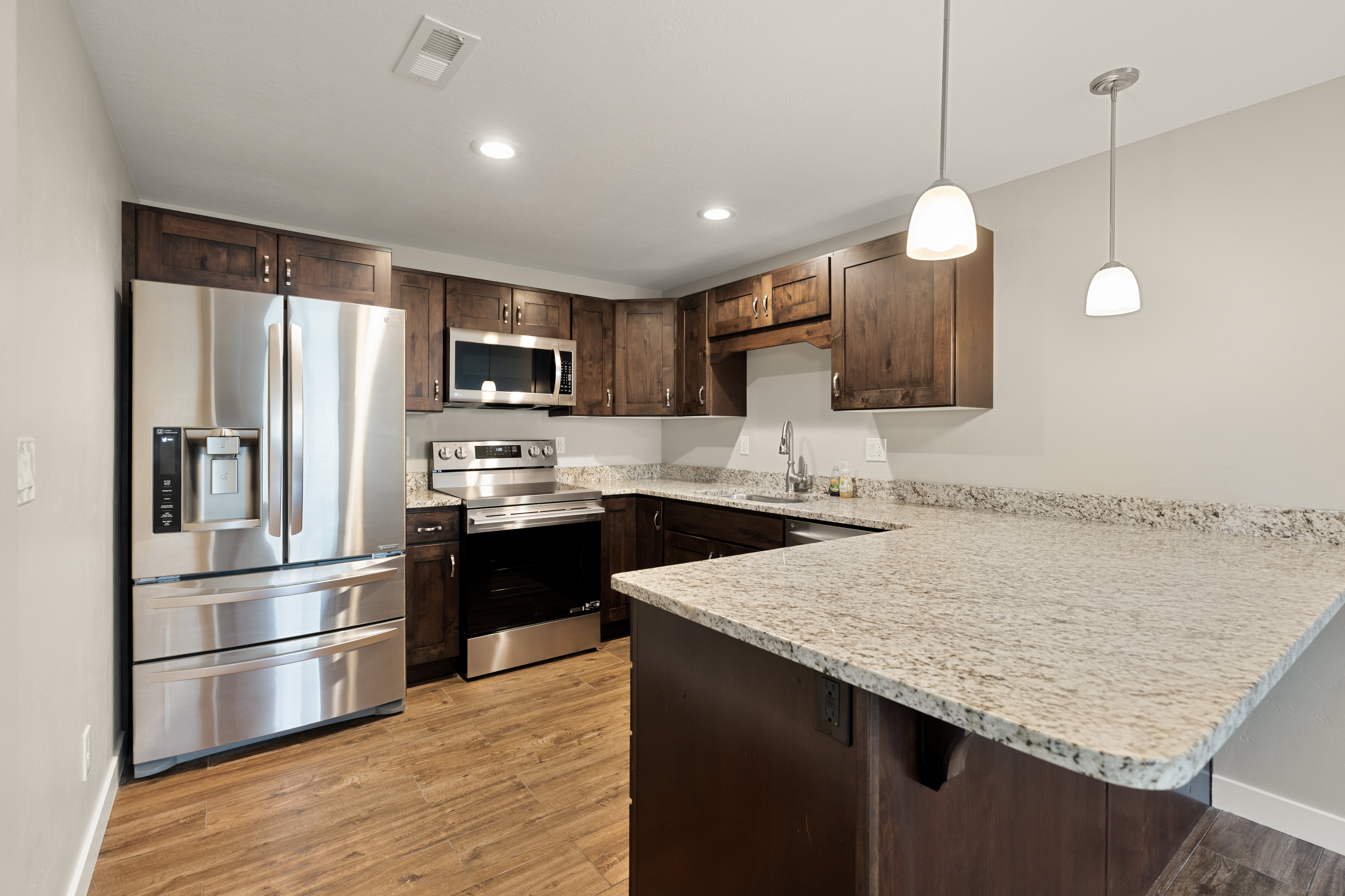 Kitchen featuring wood-finish flooring, stainless steel appliances, dark wood cabinetry, light-toned speckled countertops, and recessed lighting