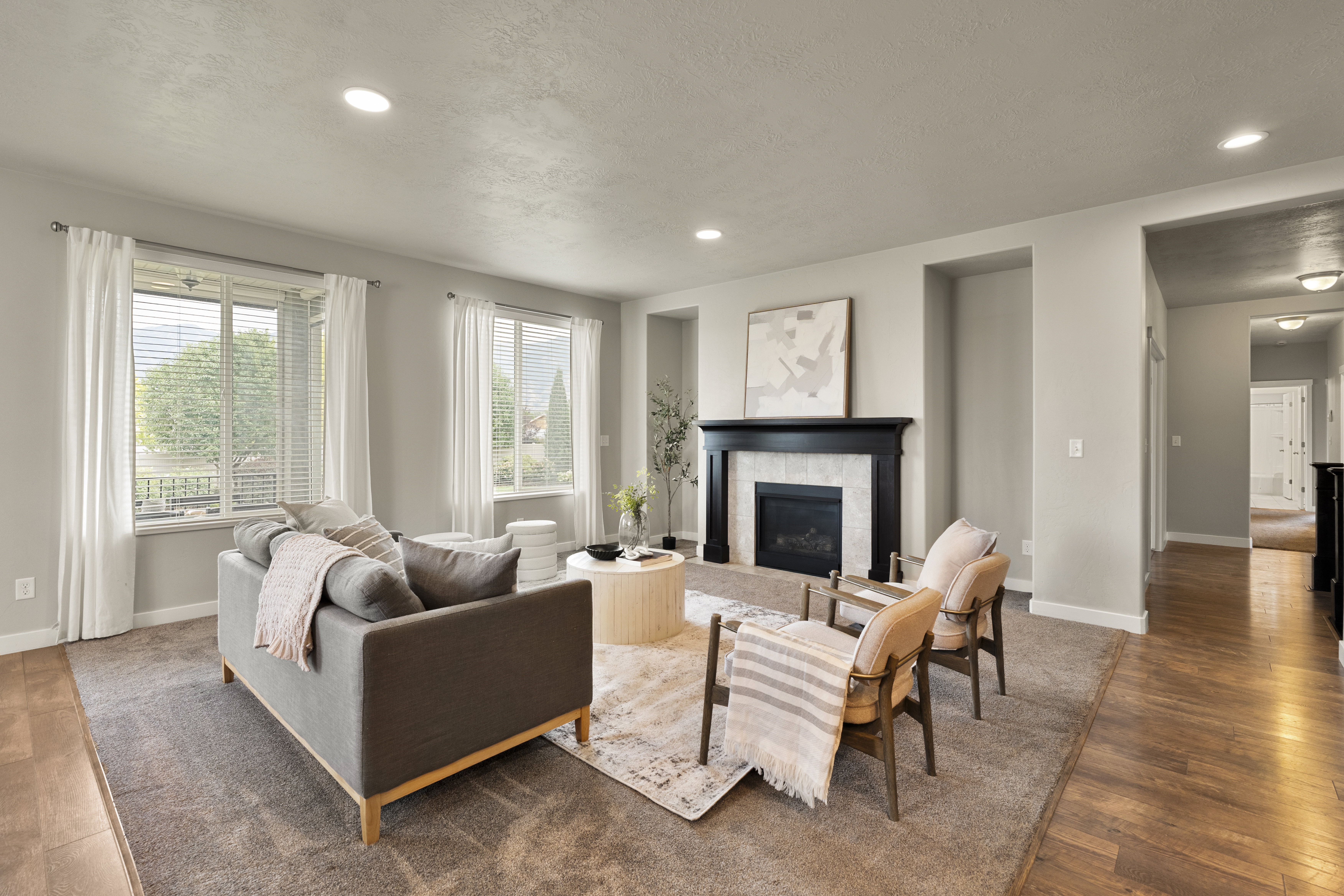 Living area featuring a dark wood mantel fireplace with a light tile surround, recessed lighting, wood-finish flooring, and multiple windows with white blinds and drapes