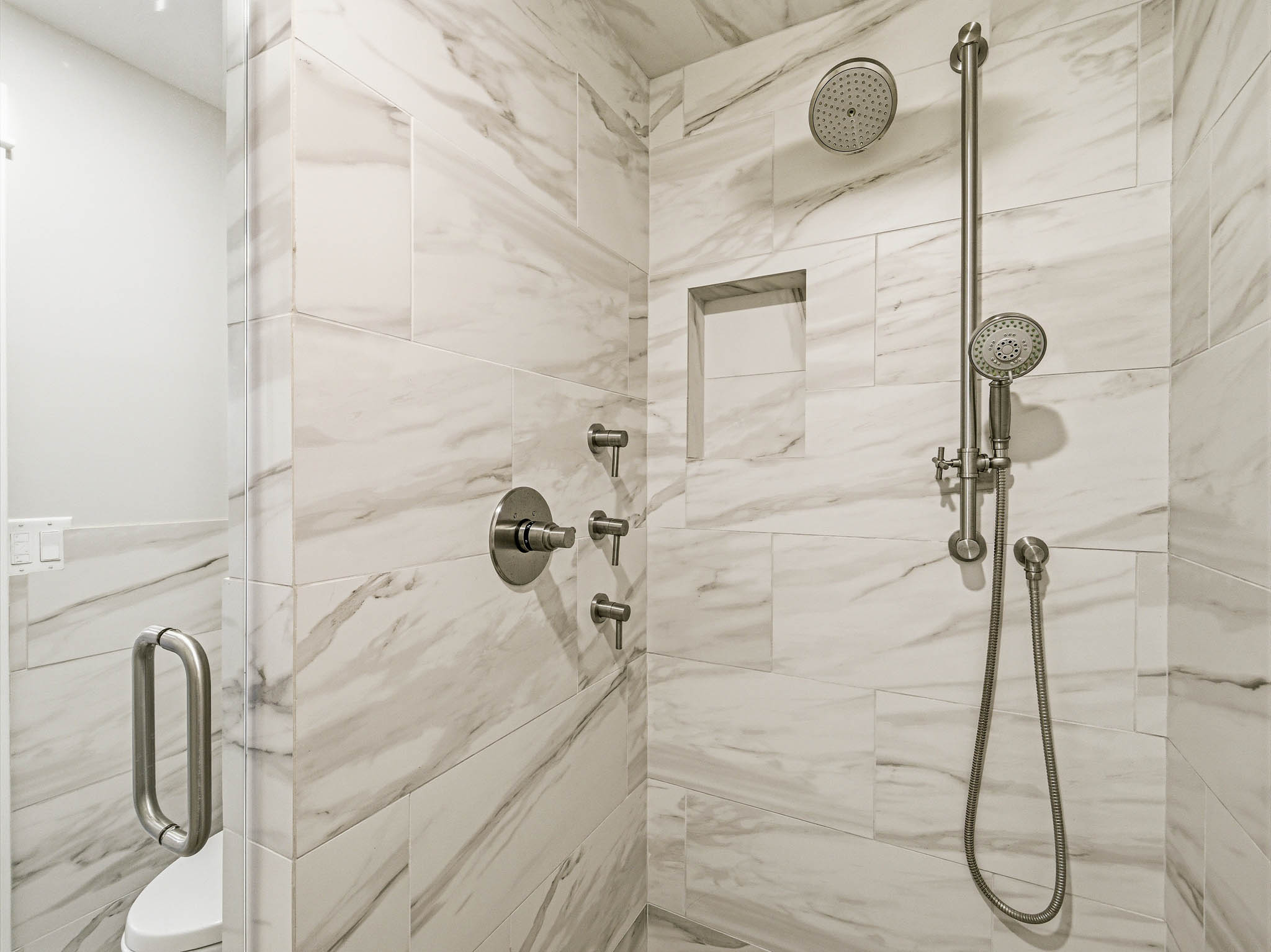 Walk-in shower featuring large format marble-look tile, rain shower head, handheld shower fixture, recessed niche, and brushed nickel hardware