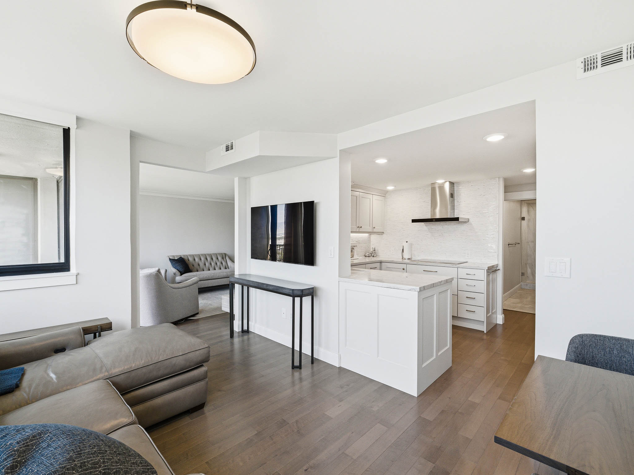 Open-concept living space featuring wood-finish flooring throughout, a modern kitchen with white cabinetry and stainless steel appliances, and recessed lighting