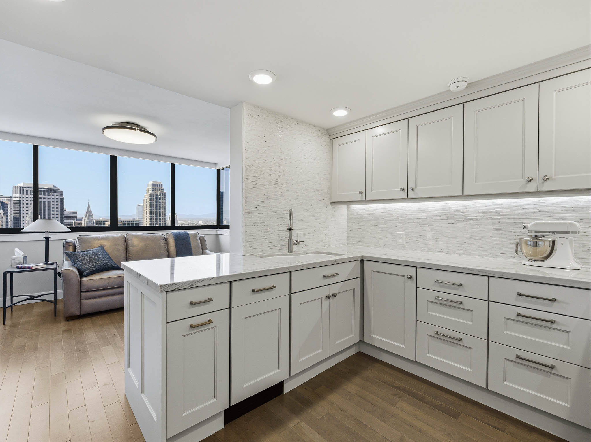 Modern kitchen featuring light gray cabinetry with brushed nickel hardware, white stone countertops, and a full-height tiled backsplash