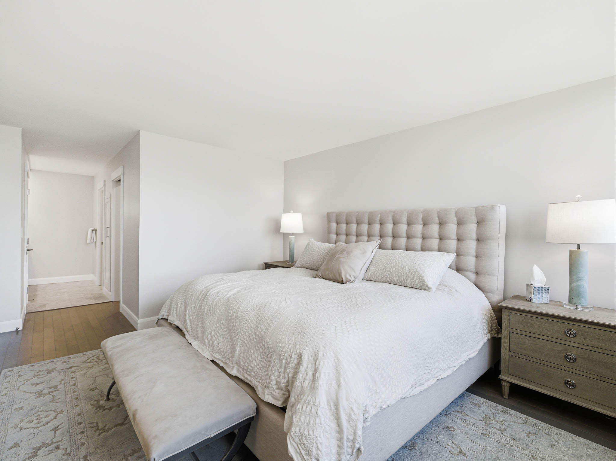 Spacious sleeping area featuring hardwood flooring, light neutral wall tones, and a plush upholstered headboard