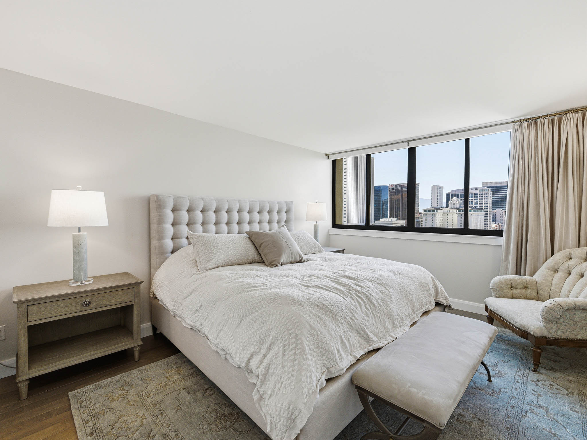 Bedroom featuring expansive windows with city buildings visible, light wood-finish flooring, and a neutral color palette