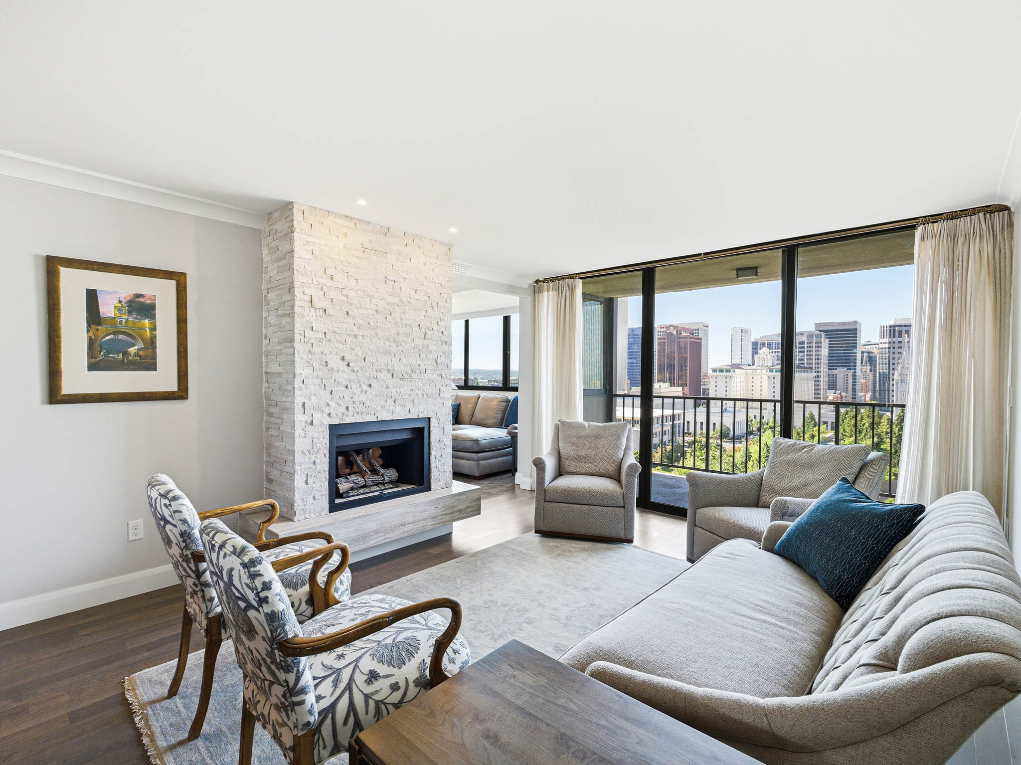 Spacious living area featuring a stacked stone fireplace, large glass panel balcony access, wood-finish flooring, recessed lighting, and crown molding
