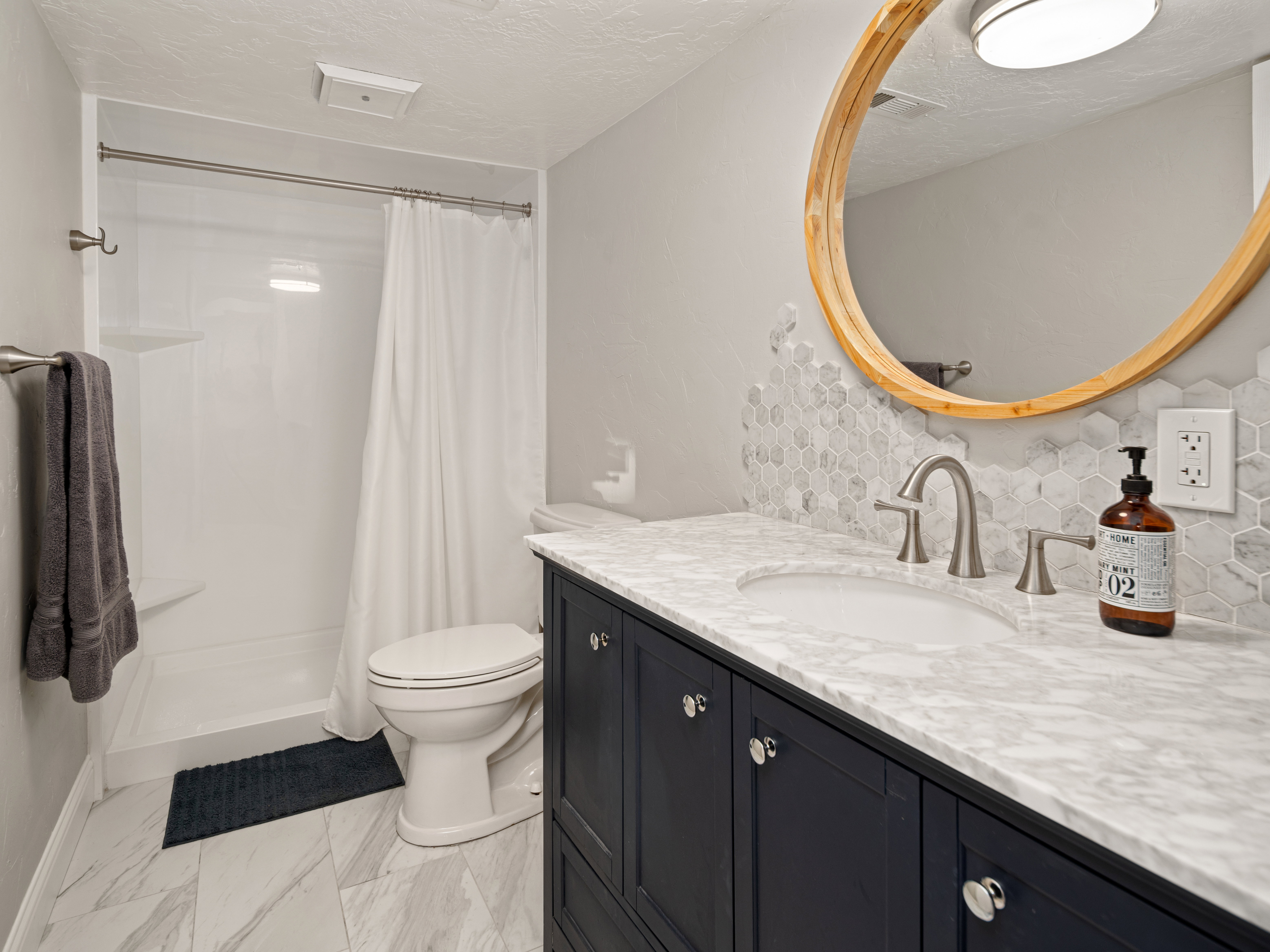 Bathroom featuring a dark blue vanity cabinet with a stone countertop and an undermount sink, complemented by a round wooden-framed mirror