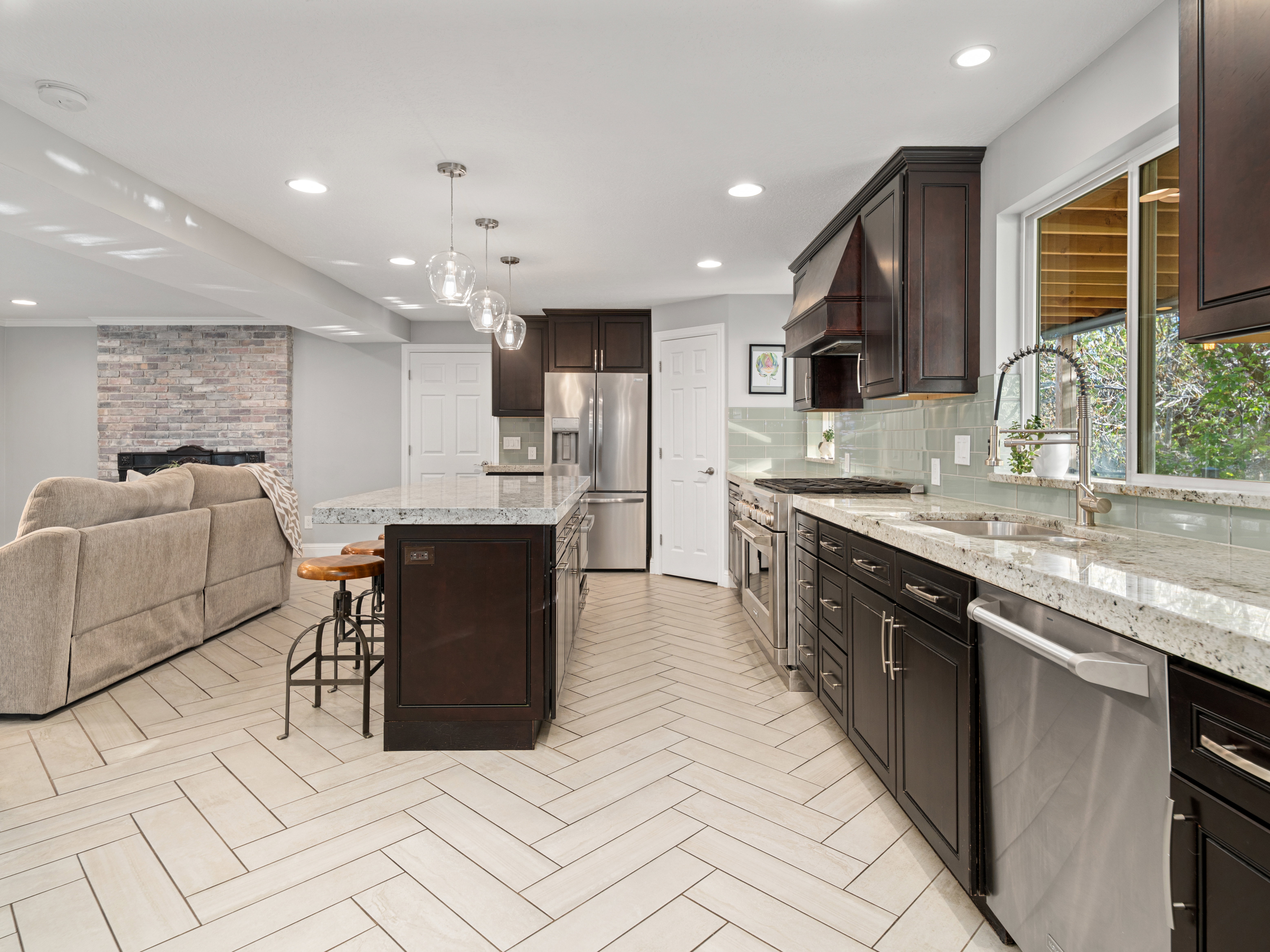 Open-concept kitchen featuring an island with pendant lighting, stainless steel appliances, granite countertops, and light tile flooring in a herringbone pattern