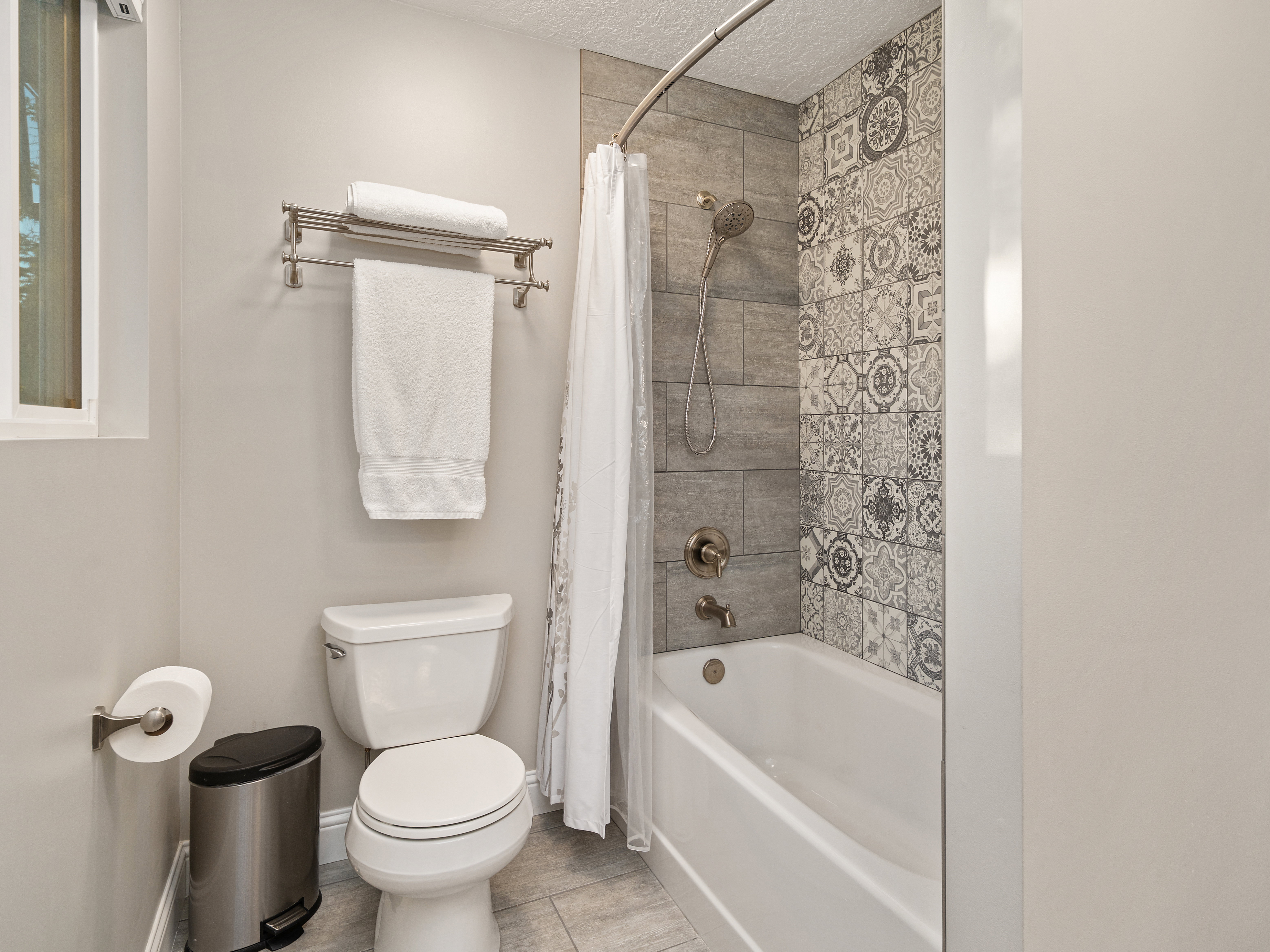 Full bathroom featuring a tub/shower combination with patterned accent tiling, a polished white toilet, and a window providing natural light