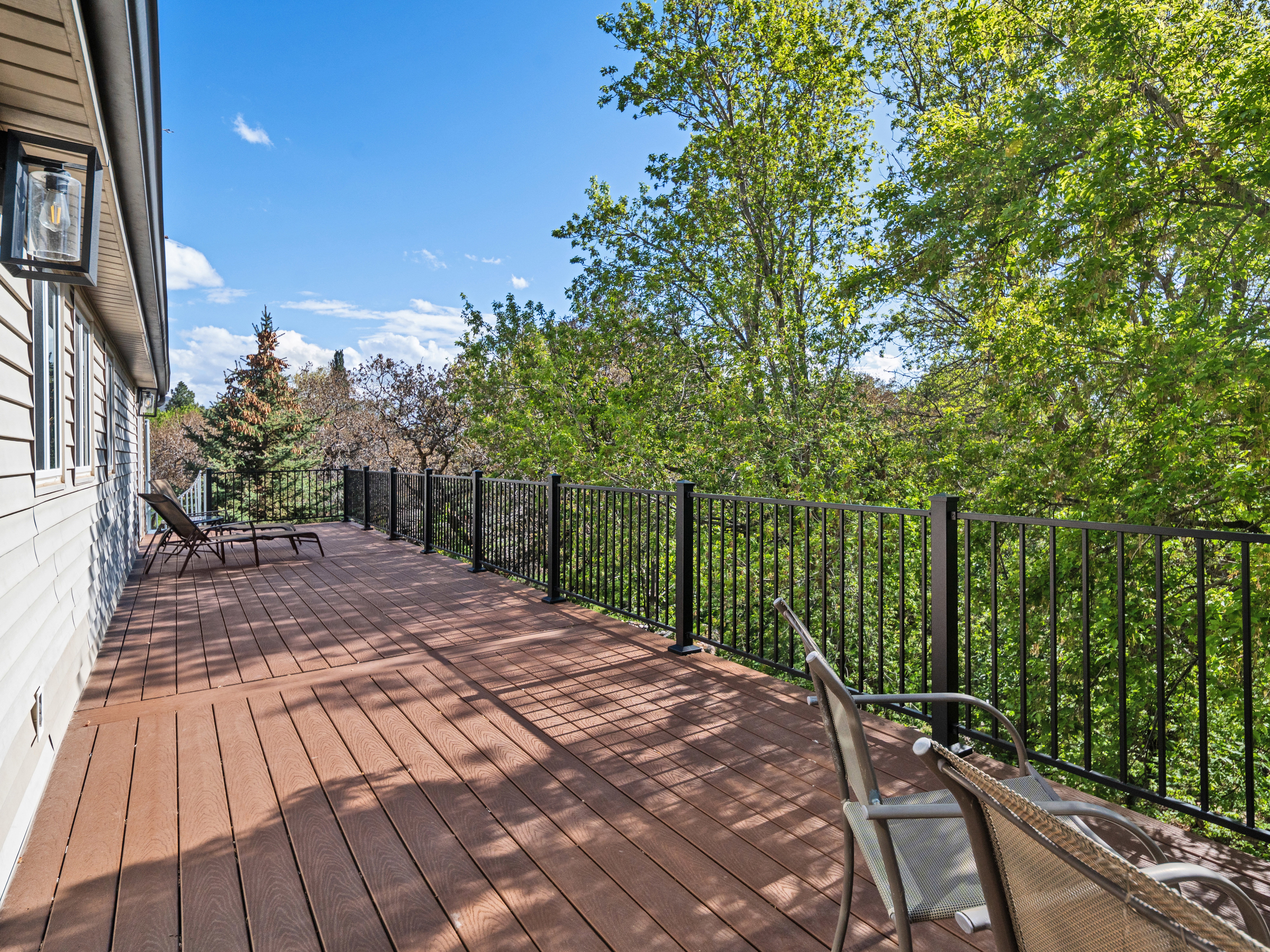 Expansive outdoor deck featuring wood-finish flooring, black metal railings, and attached exterior lighting